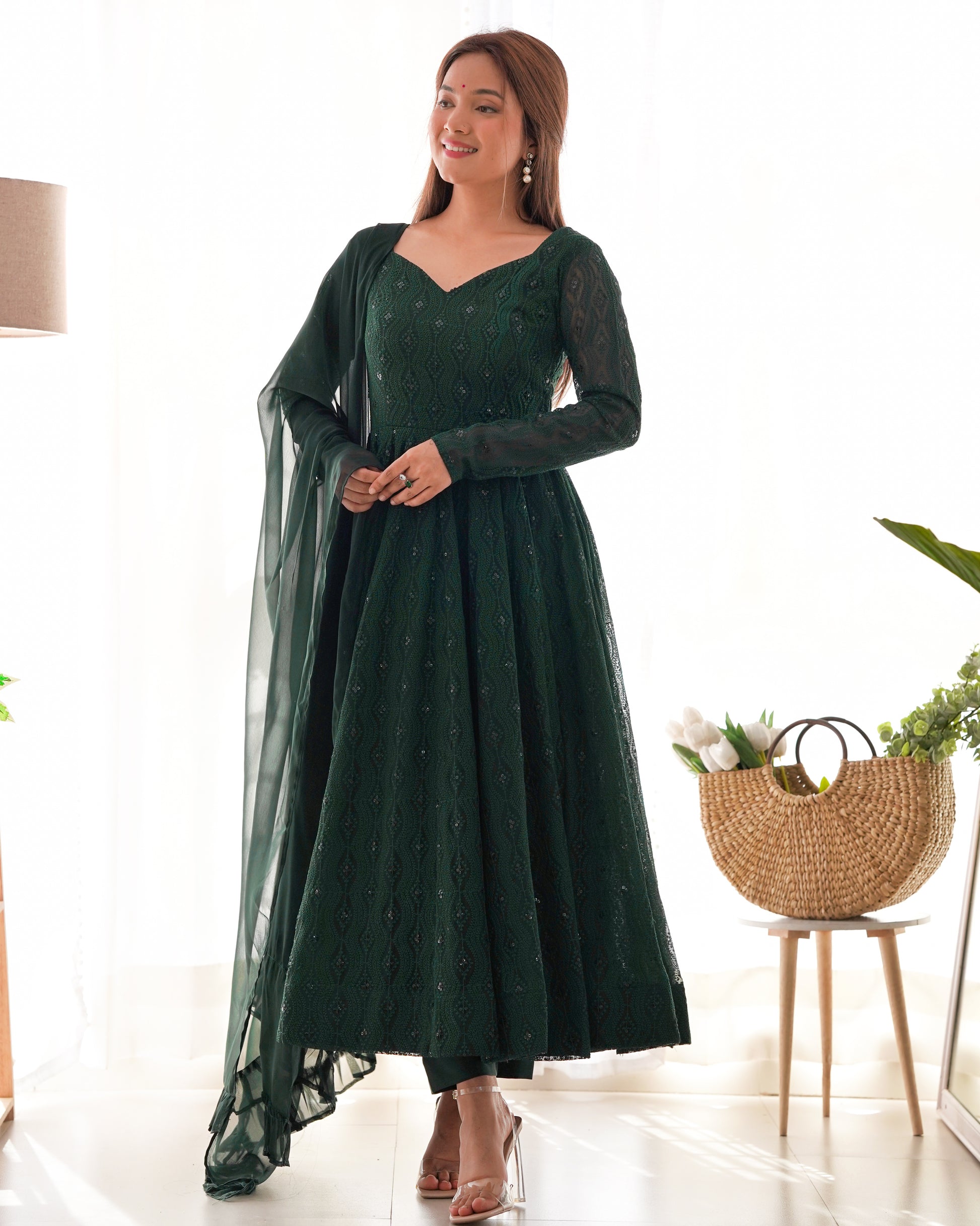 Woman wearing a green dress with a sheer overlay in a bright room.