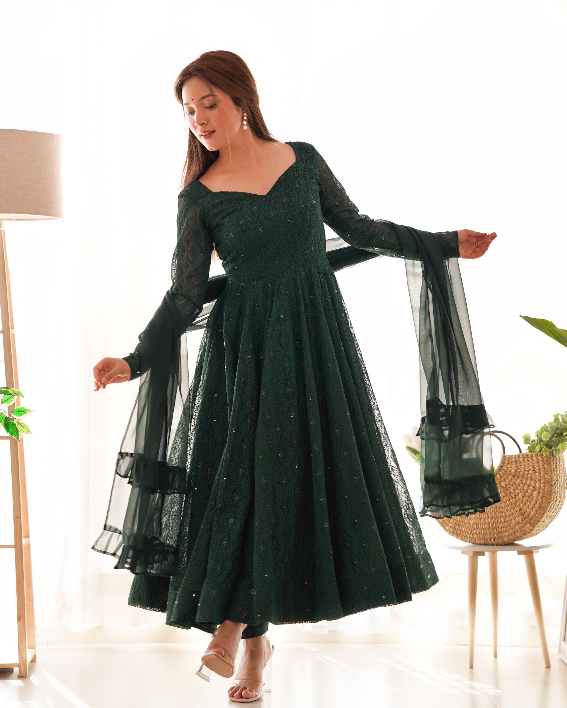 Woman wearing a dark green dress with sheer sleeves in a bright room.