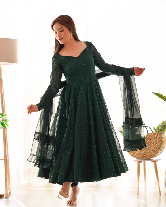 Woman wearing a dark green dress with sheer sleeves in a bright room.