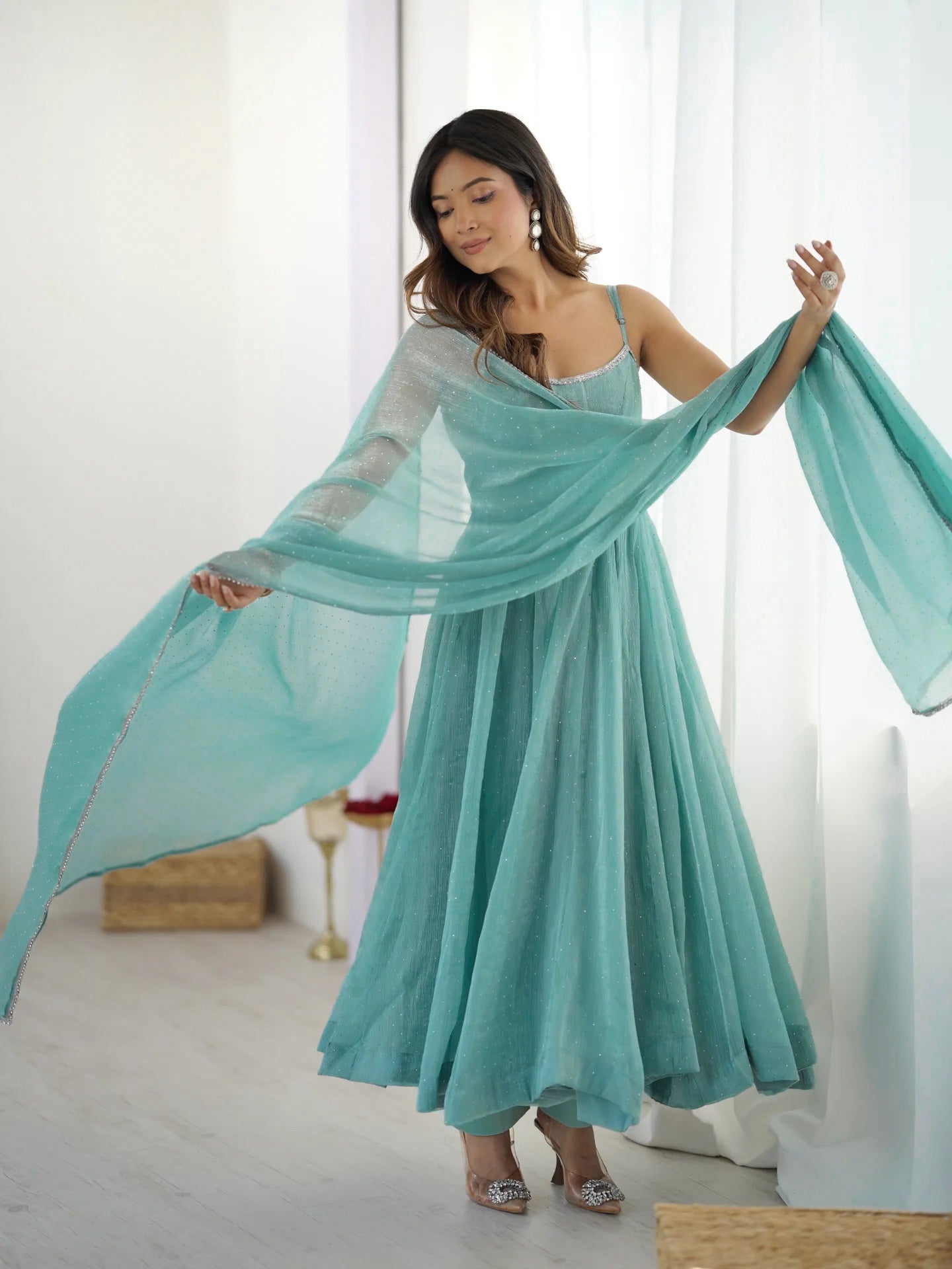 Woman wearing a light blue dress with a sheer overlay in a bright room.