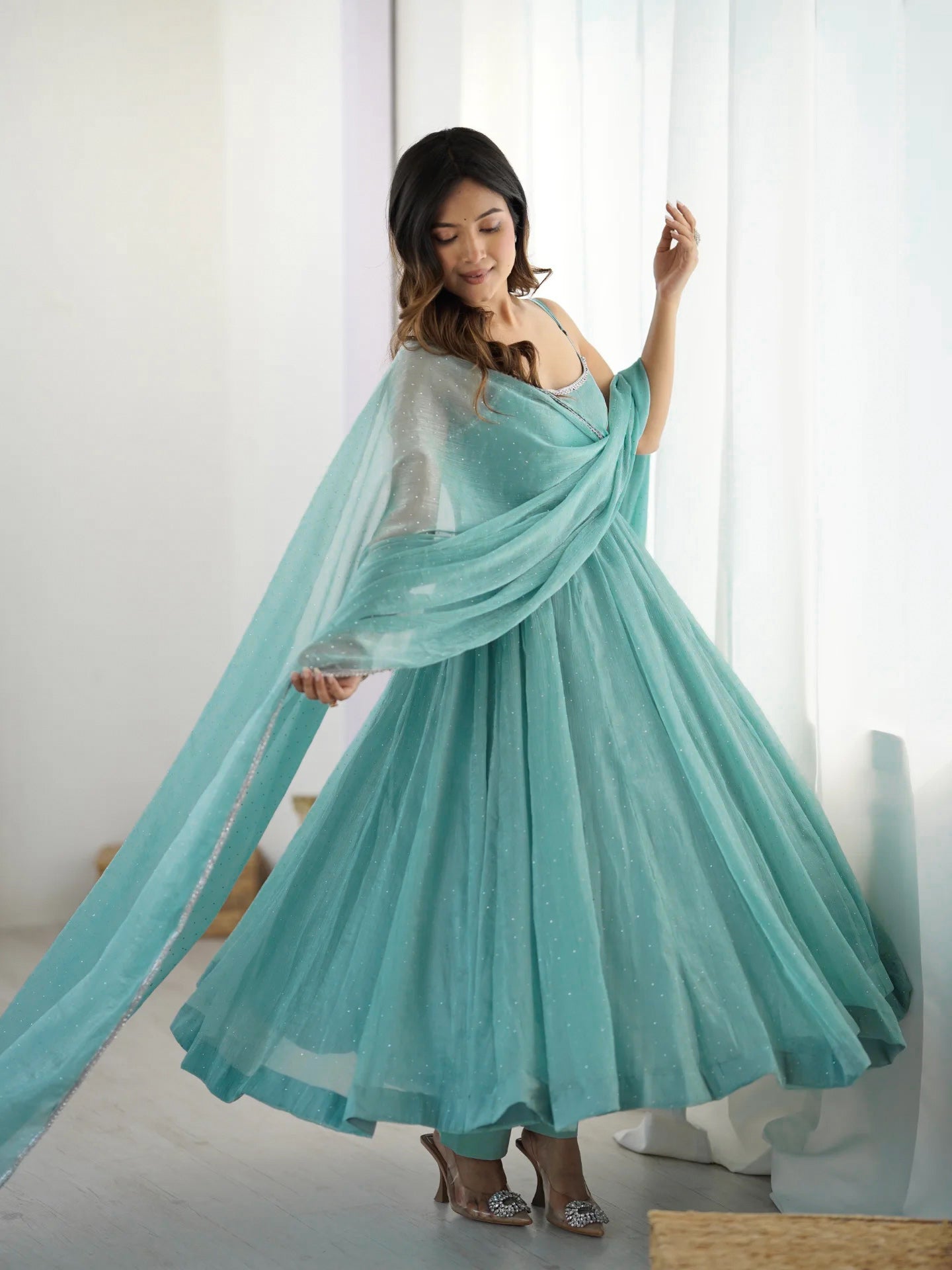 Woman wearing a flowing turquoise dress in a bright room.