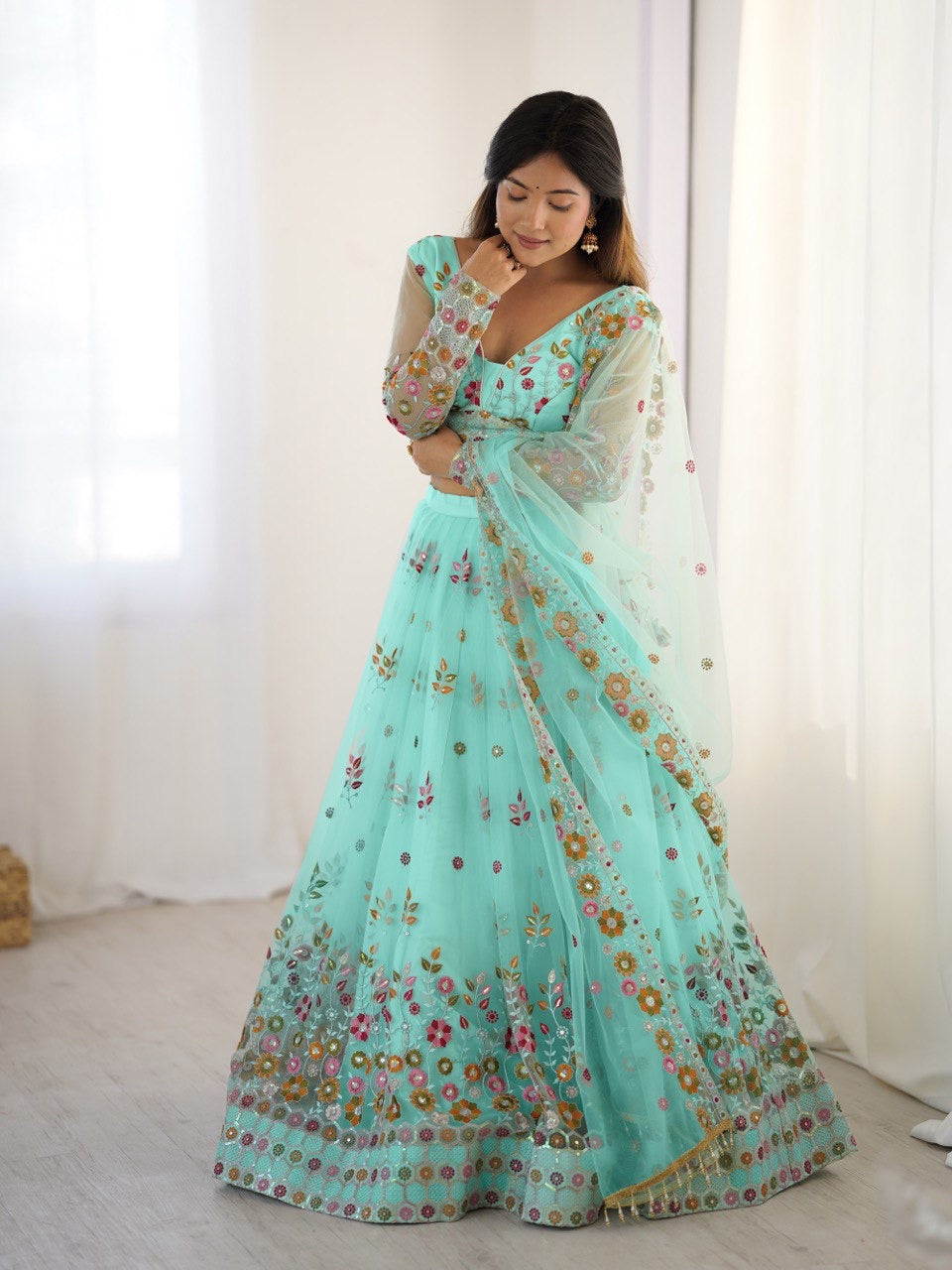 Woman wearing a light blue saree with floral patterns in a minimal indoor setting