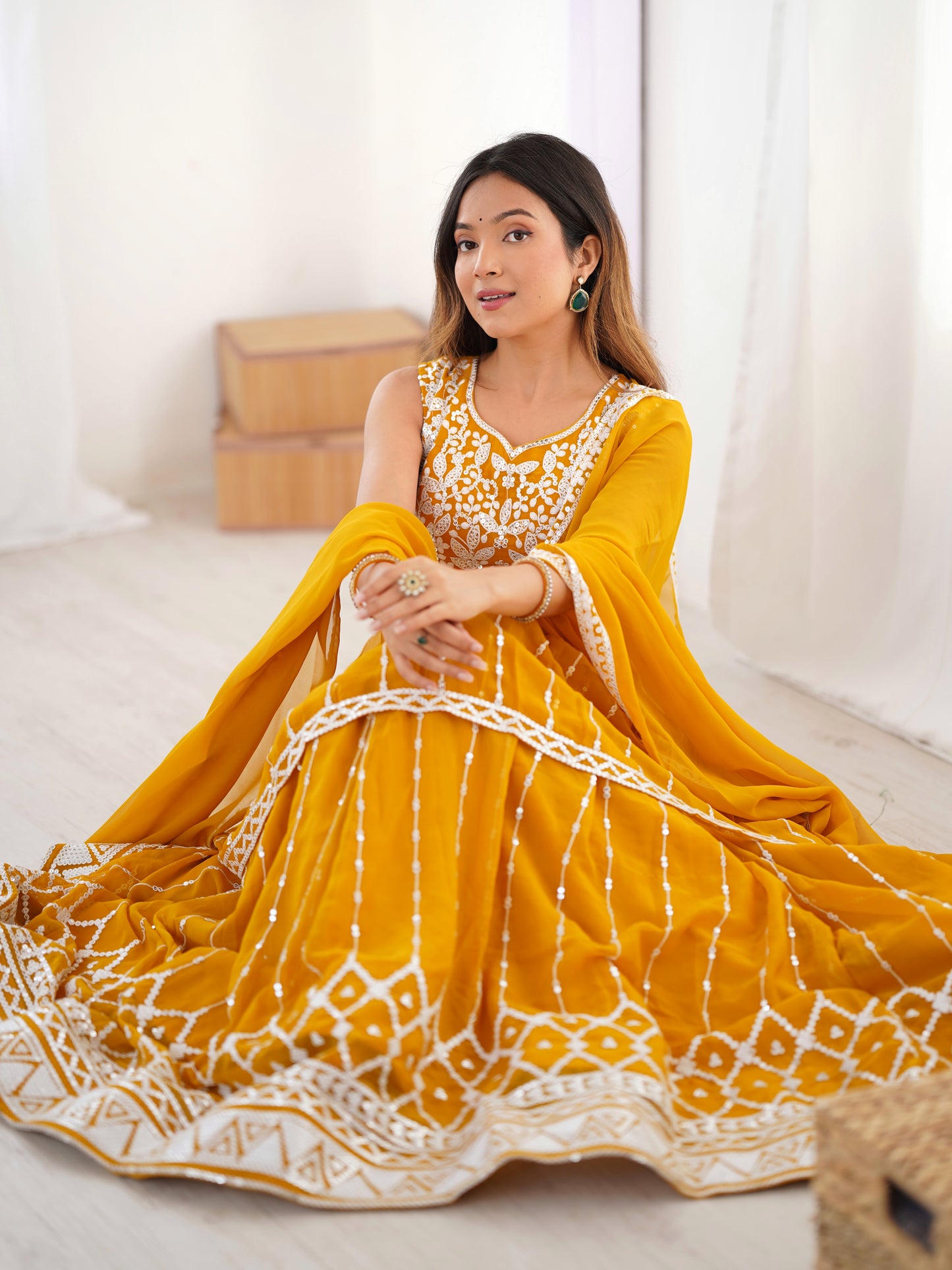 Woman wearing a yellow traditional outfit with white patterns sitting on a light-colored couch.