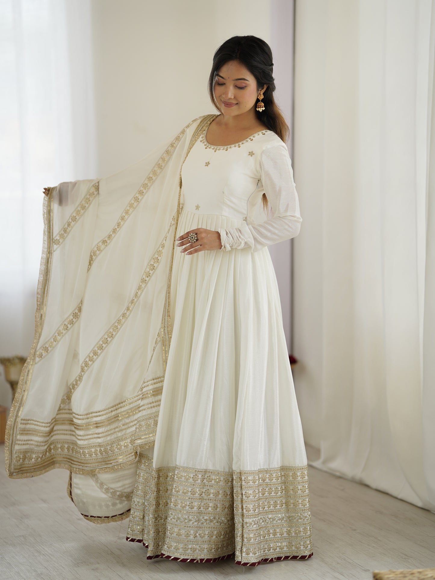 Woman wearing a white traditional outfit with gold embroidery against a plain background