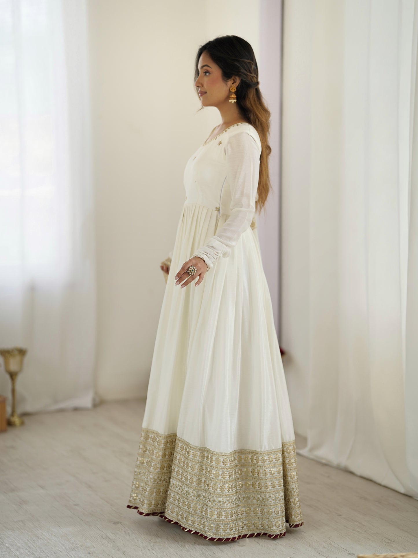 Woman wearing a white dress with gold trim against a white curtain background