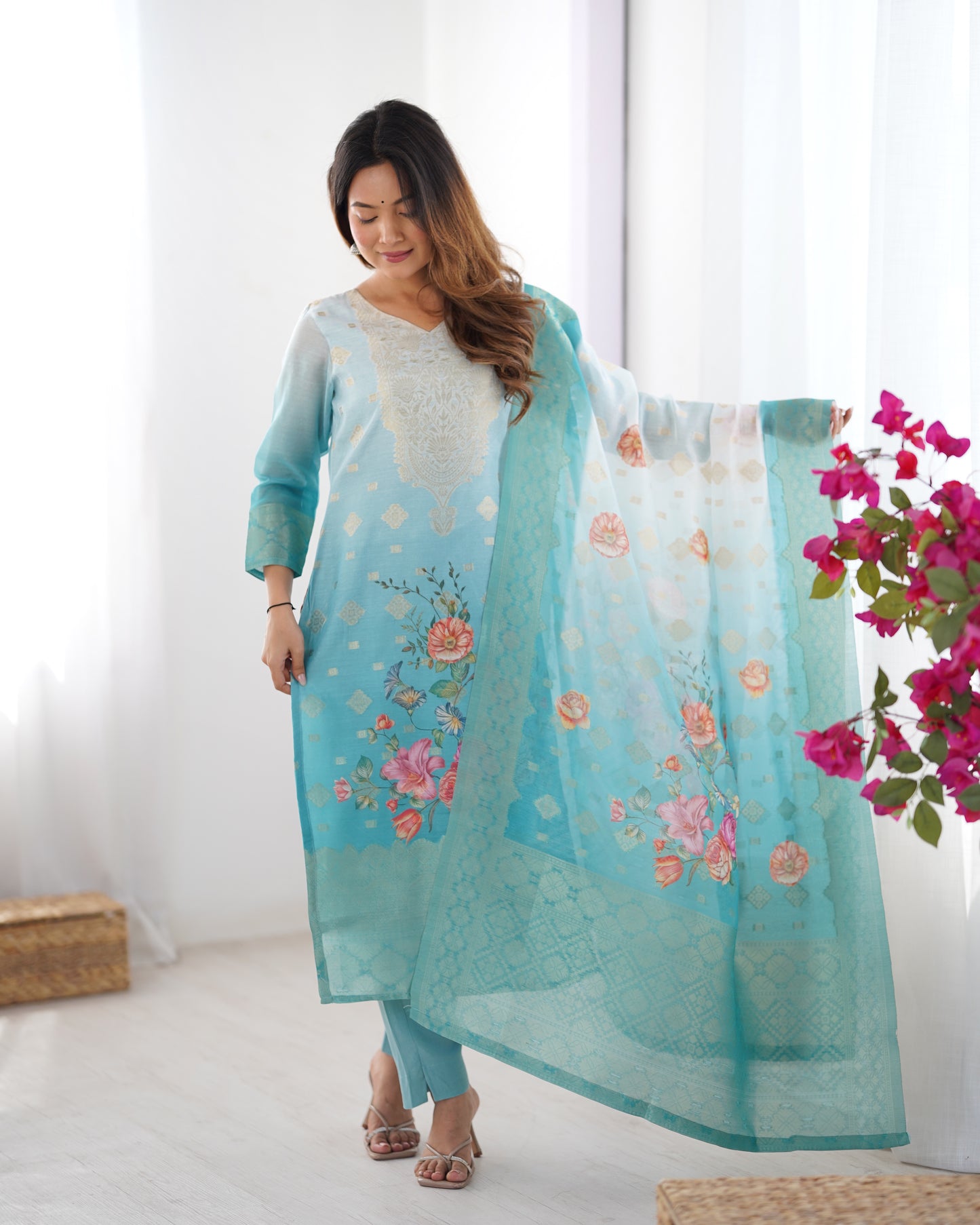 Woman wearing a light blue floral embroidered outfit with a matching dupatta, standing indoors.