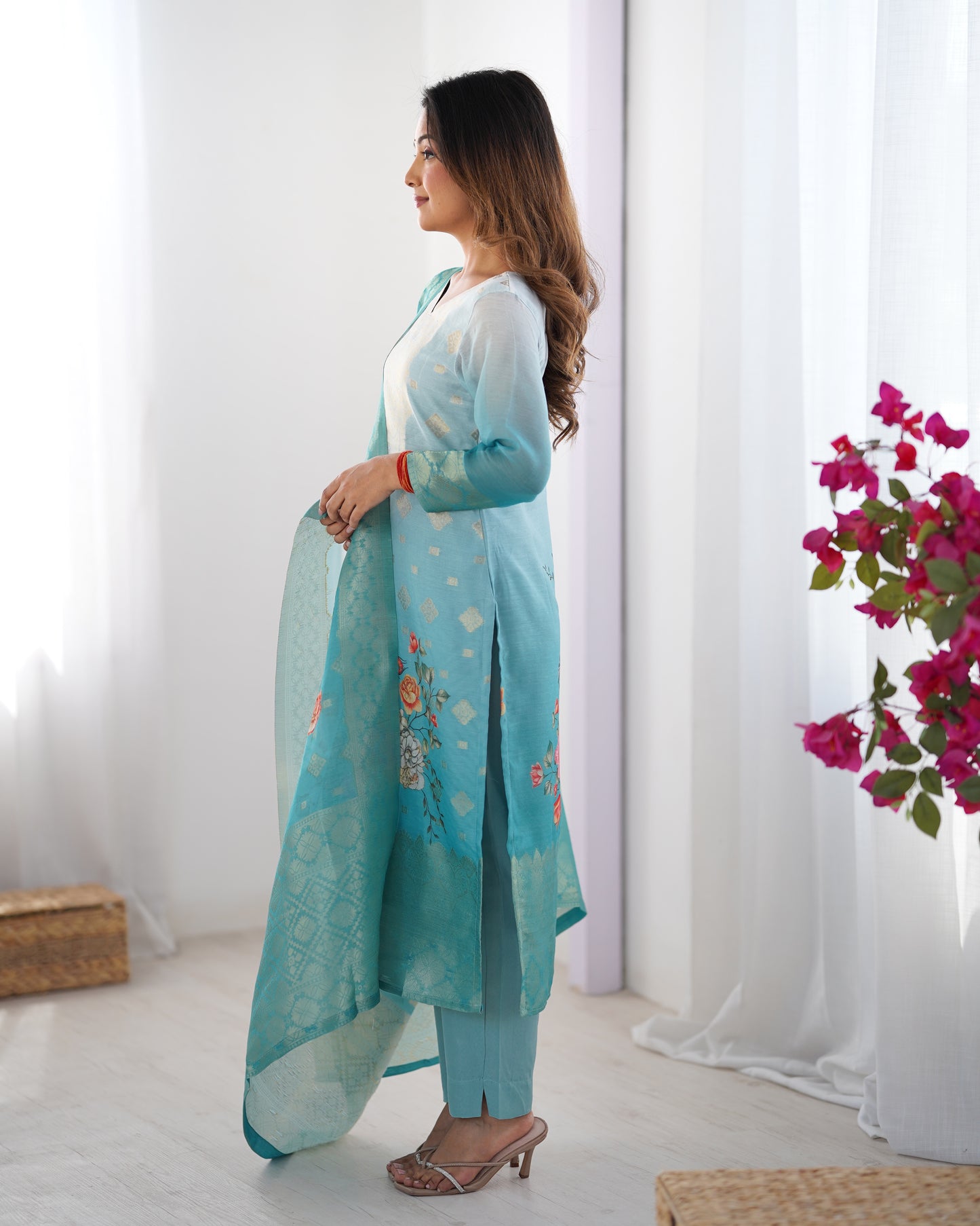 Woman in a light blue traditional outfit with a white background and flowers.