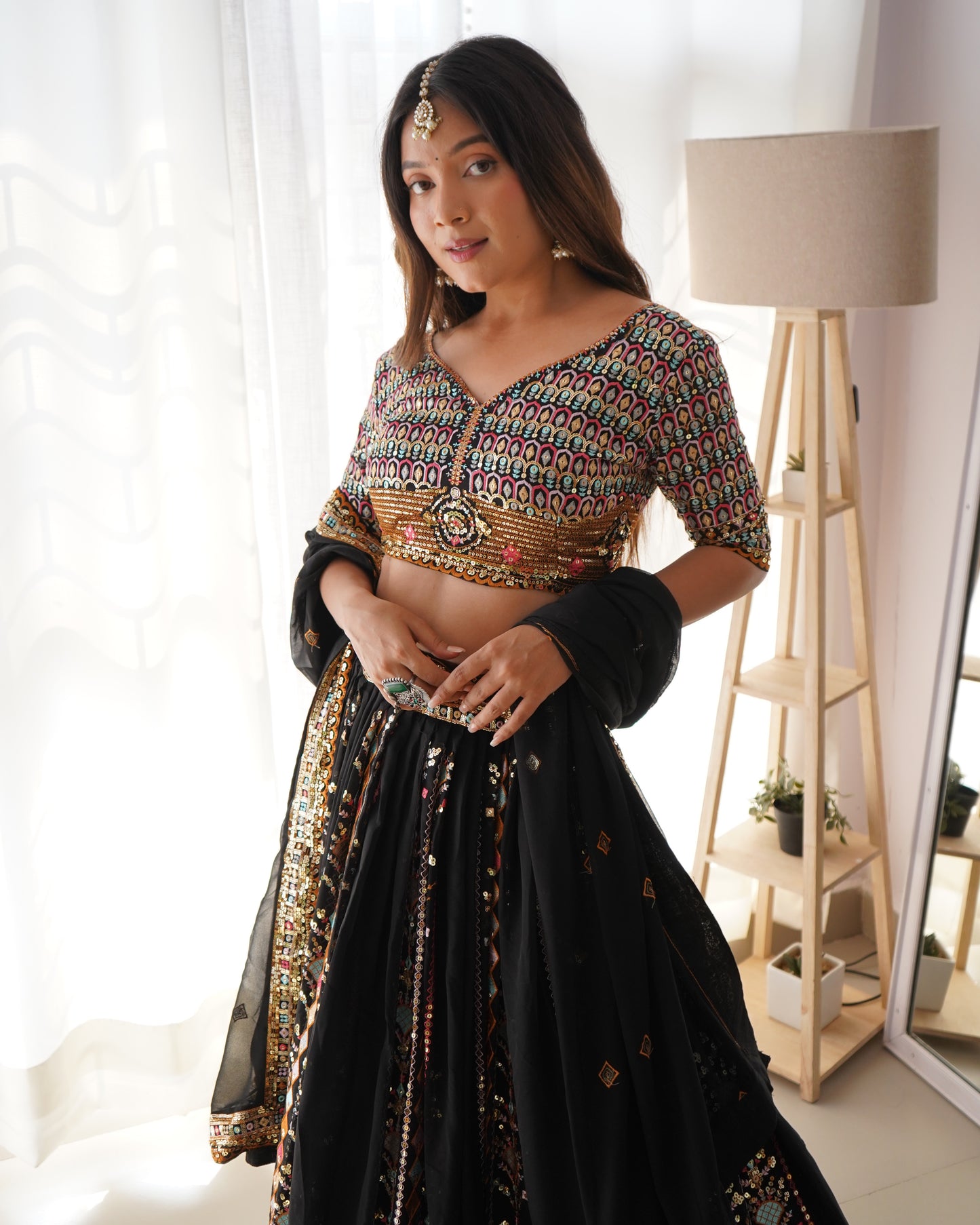 Woman wearing a traditional outfit with a colorful top and black skirt in a well-lit room.