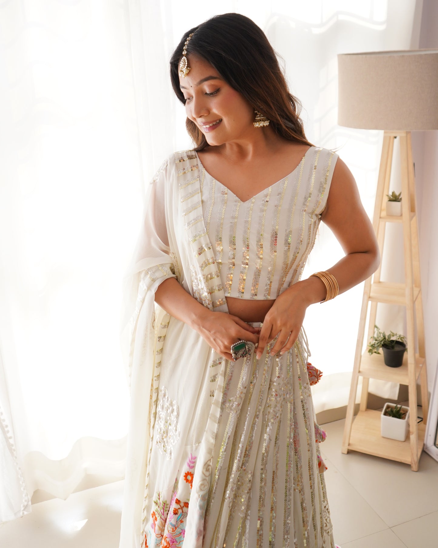 Woman in a white and gold traditional outfit standing in a bright room.