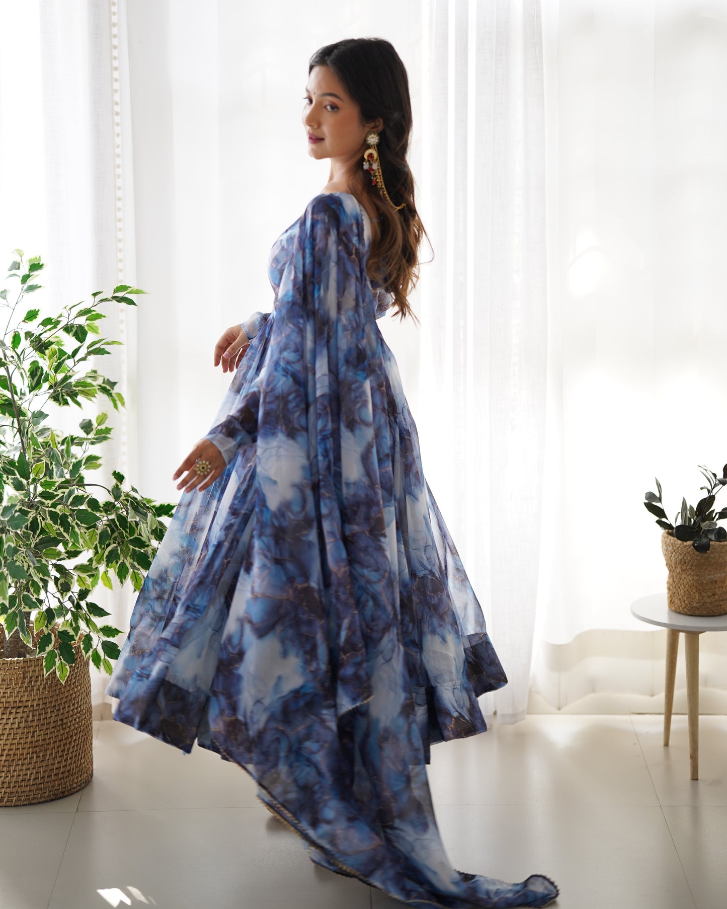 Woman wearing a blue and white patterned dress standing in a bright room with plants.