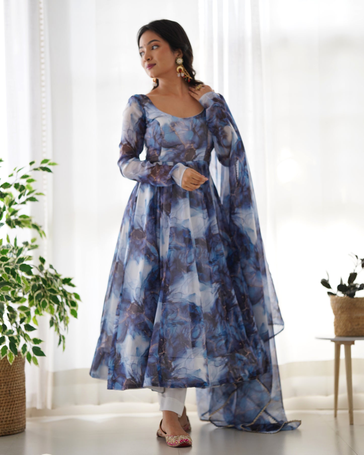 Woman wearing a blue and white patterned dress standing in a bright room with plants.