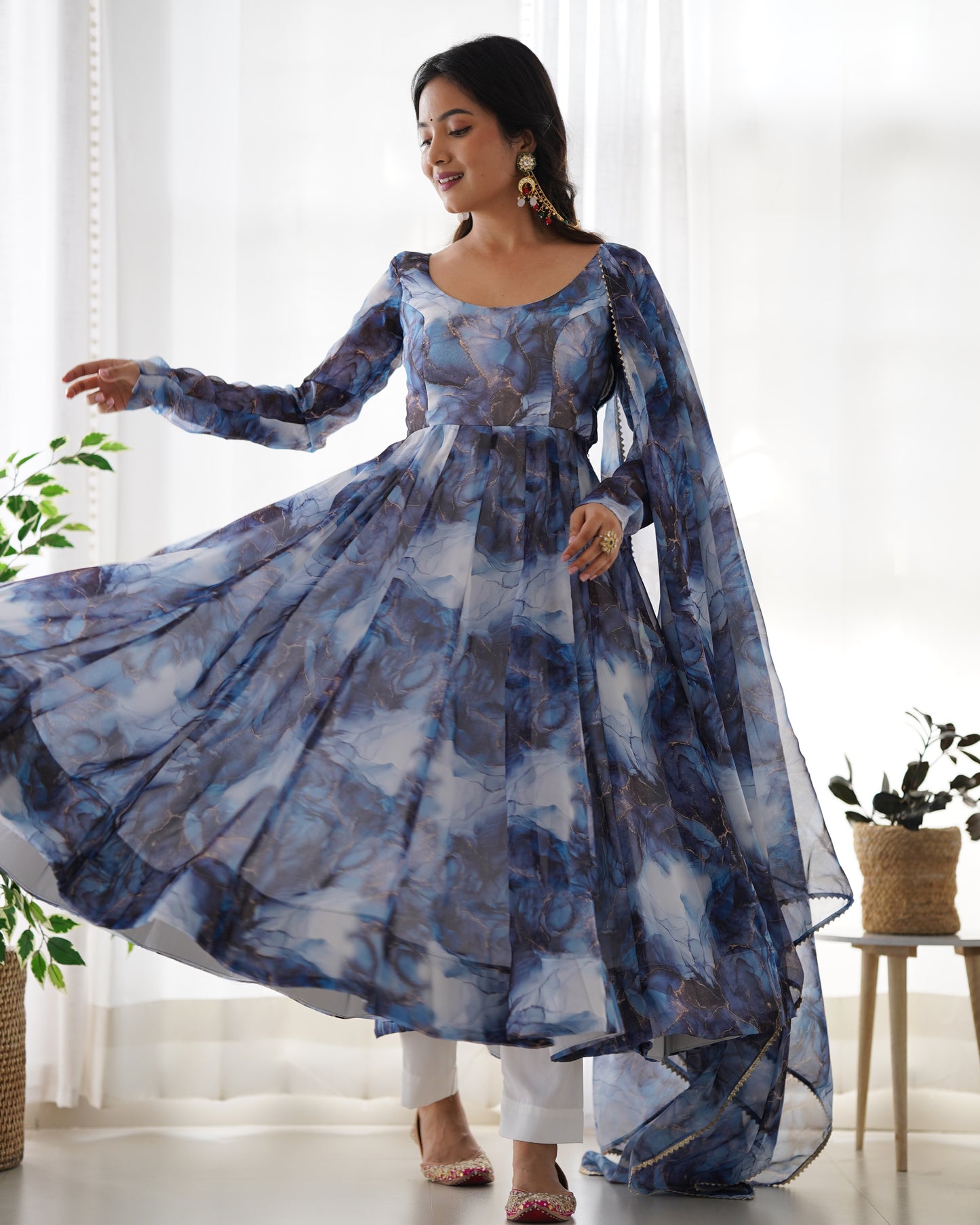 Woman wearing a blue floral dress in a bright room with plants.
