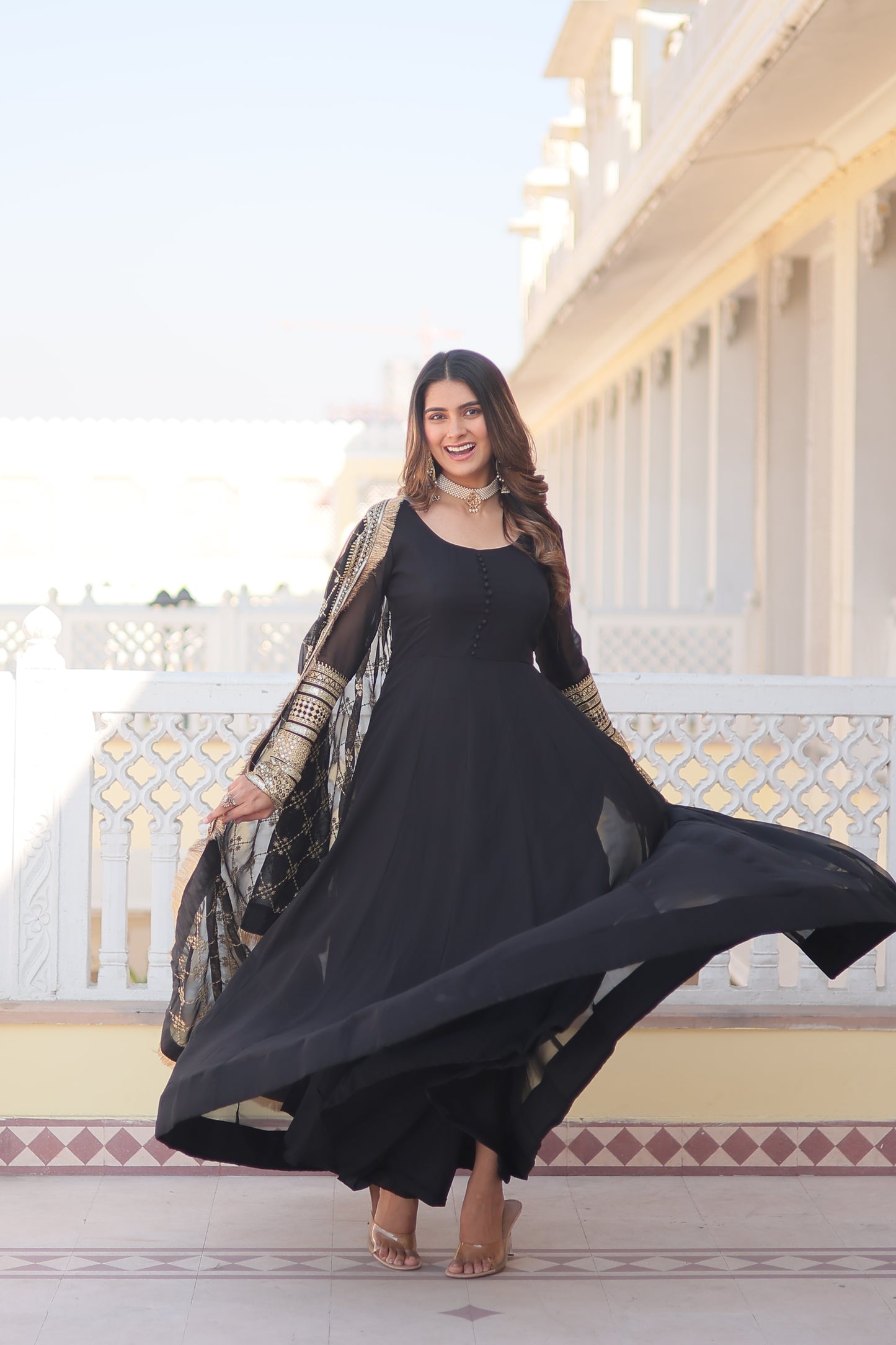 Woman in a black dress standing on a staircase with a decorative wall in the background