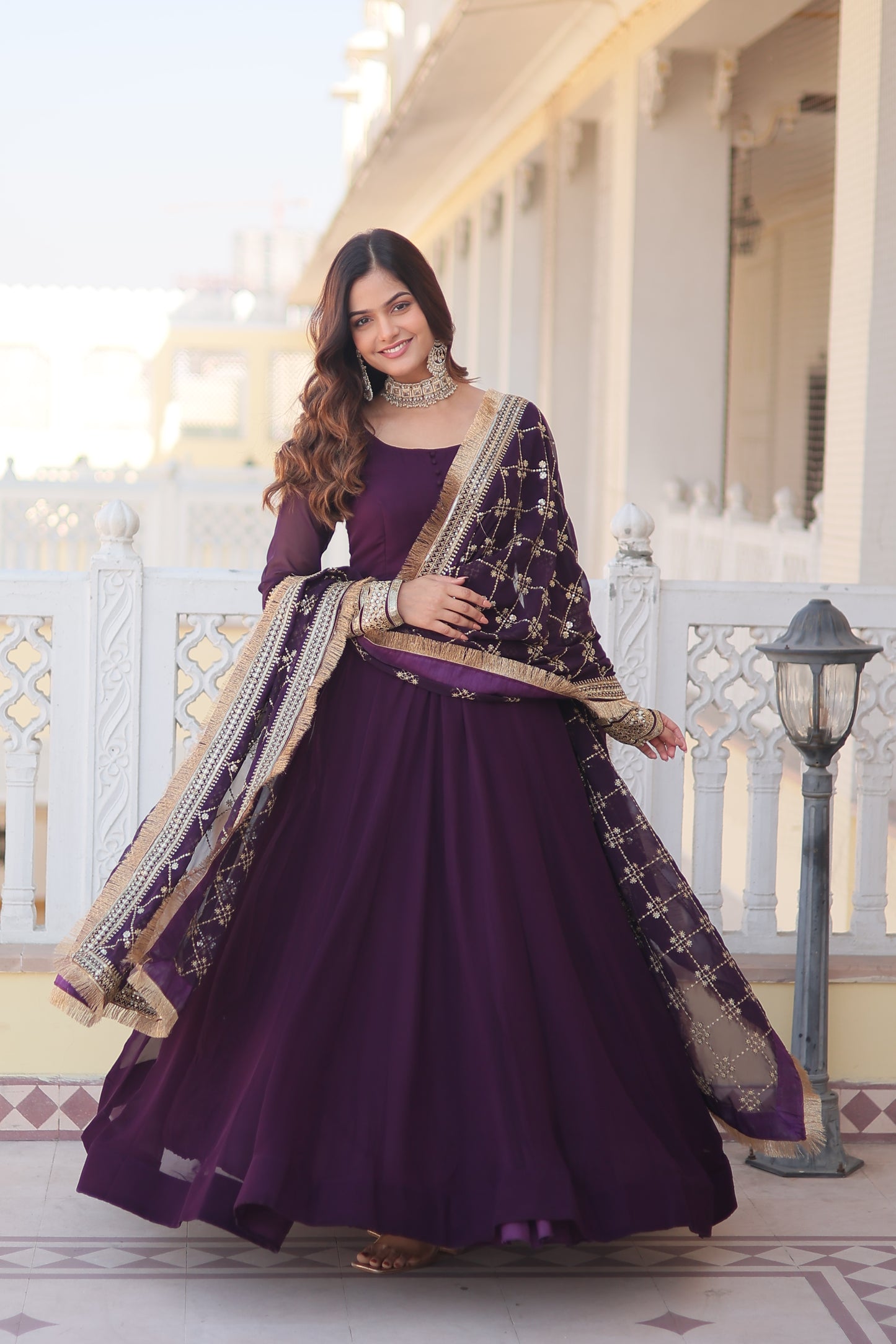 Woman in a purple traditional outfit standing in a decorative interior setting.