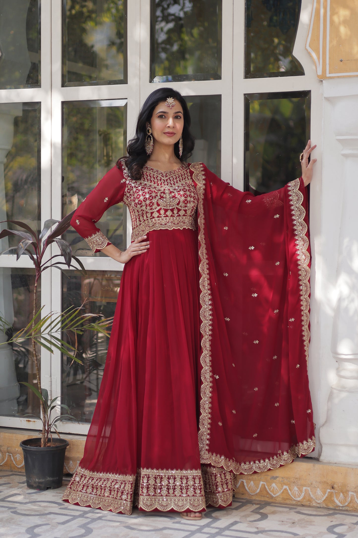 Woman wearing a red traditional outfit with gold embroidery indoors.