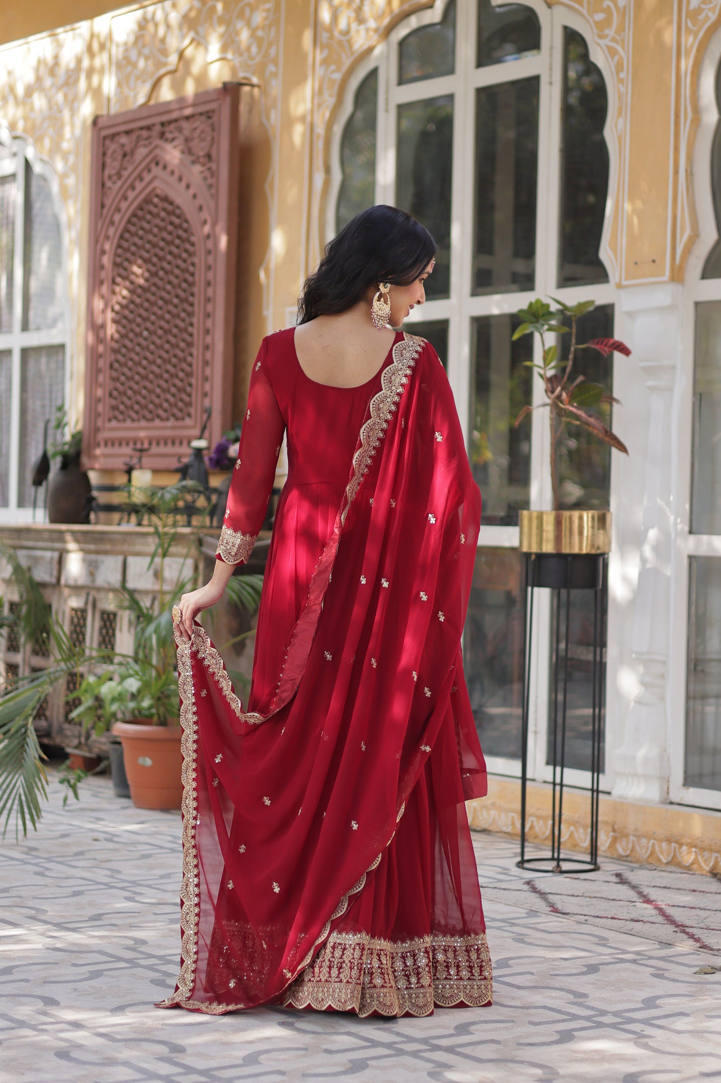 Person wearing a red traditional outfit with intricate designs indoors.