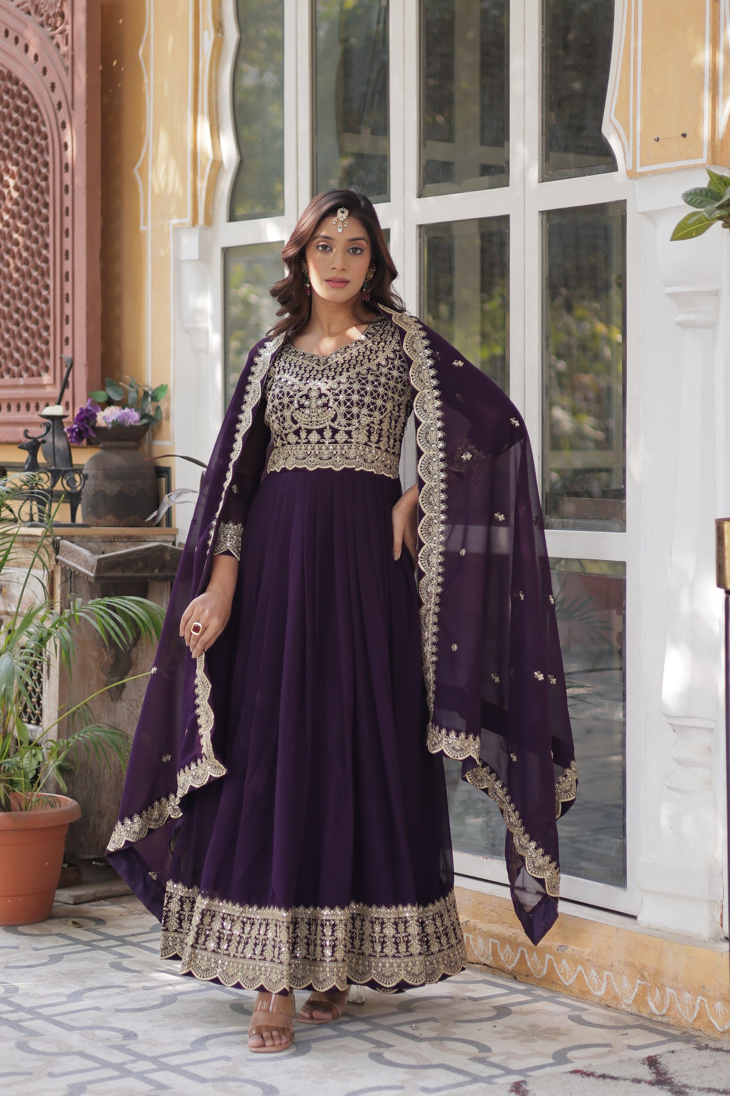 Woman wearing a purple traditional outfit with white embroidery indoors.
