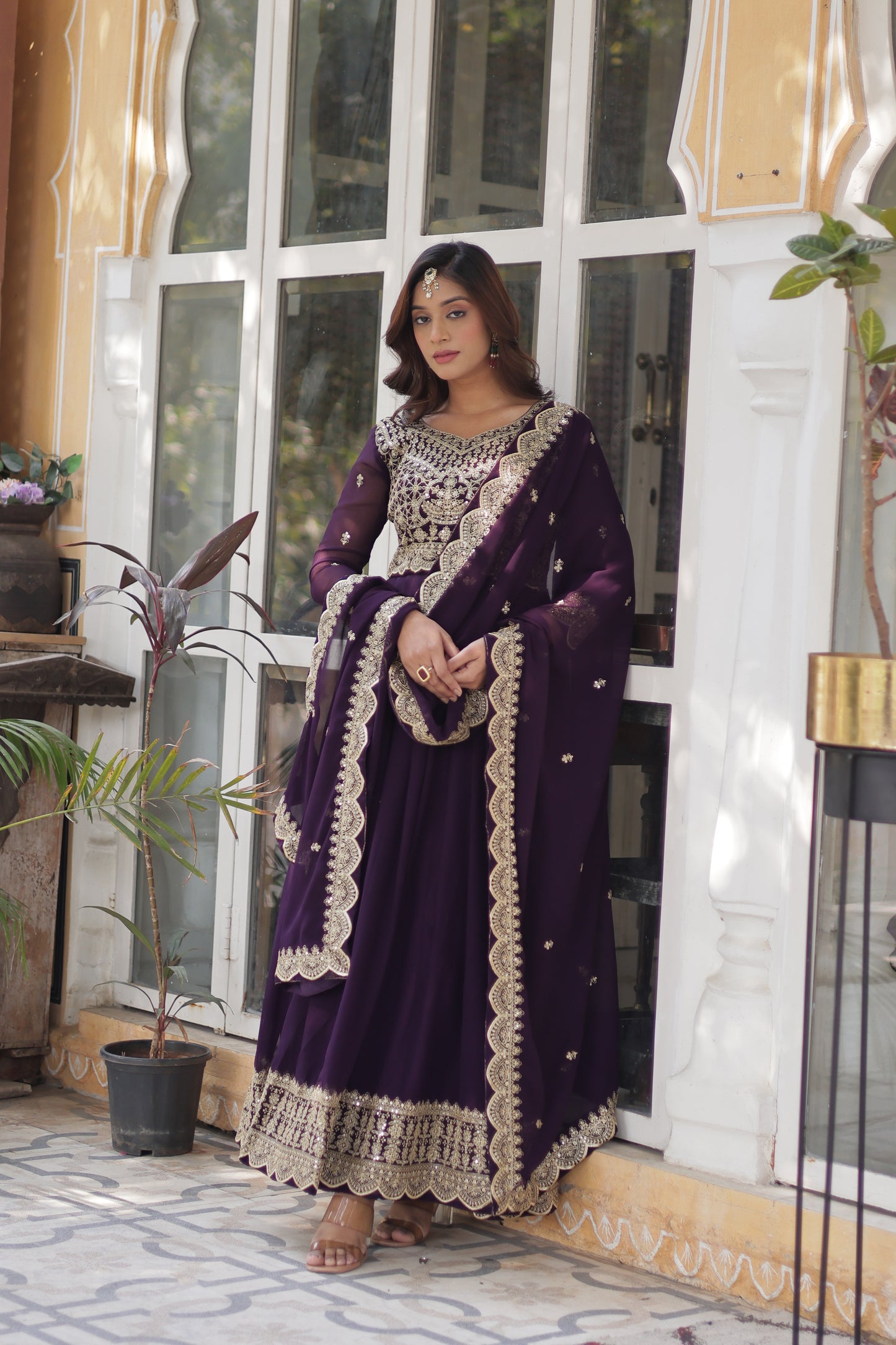 Woman in a purple dress with white embroidery standing in front of a glass door.