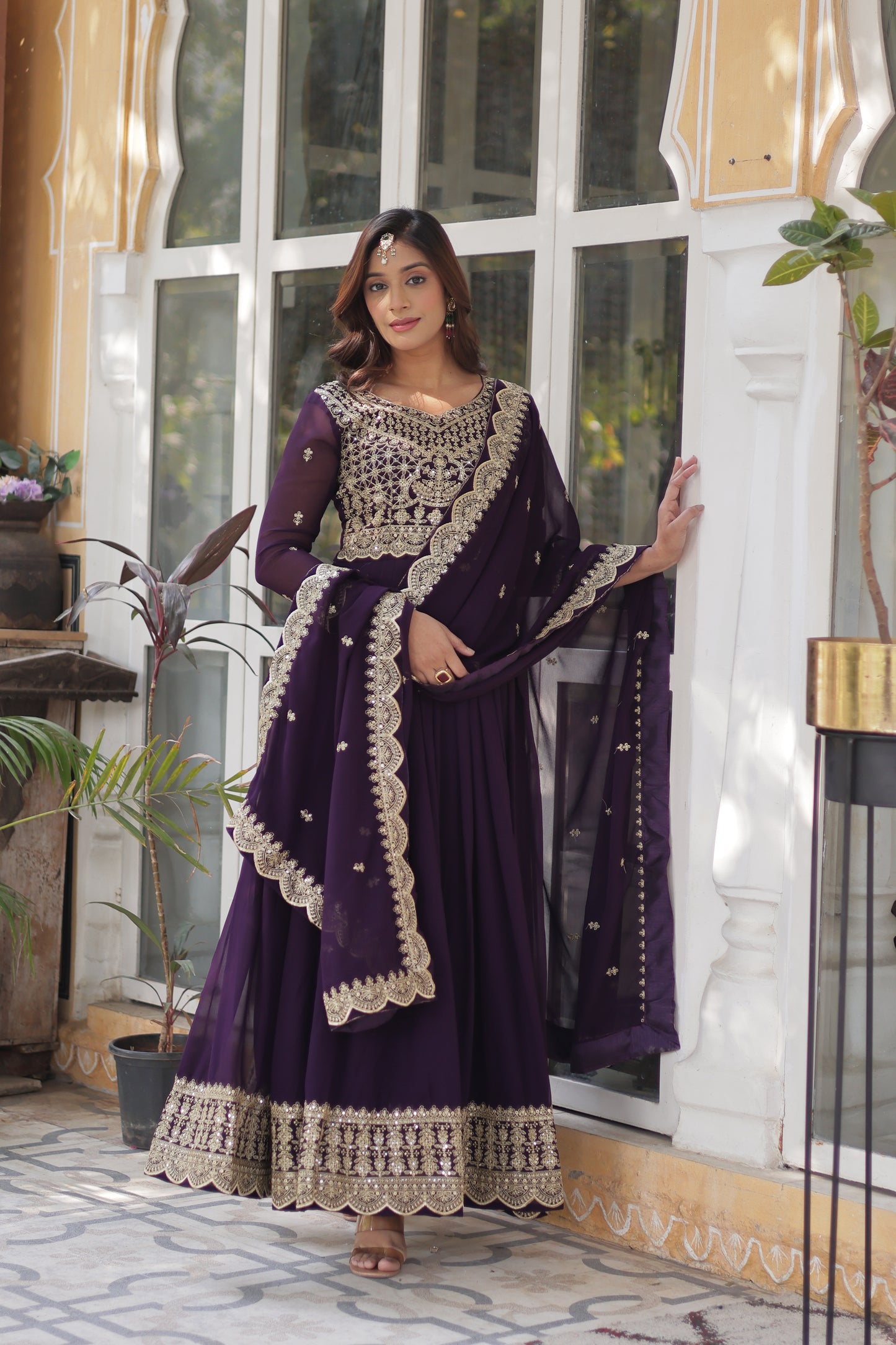 Woman wearing a purple dress with white embroidery in a room with glass doors.
