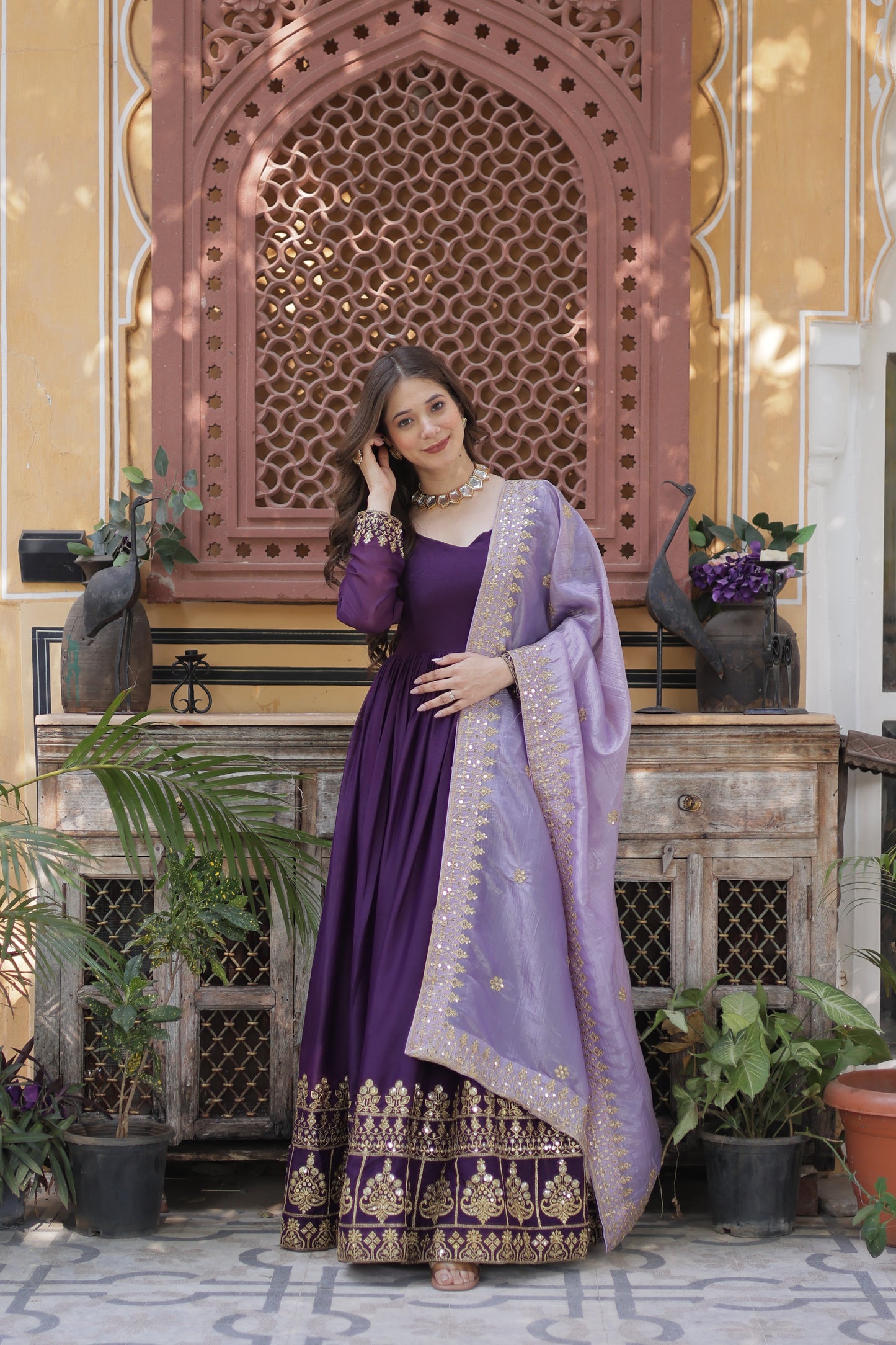 Woman in a purple dress with gold embroidery standing in front of a decorative archway.