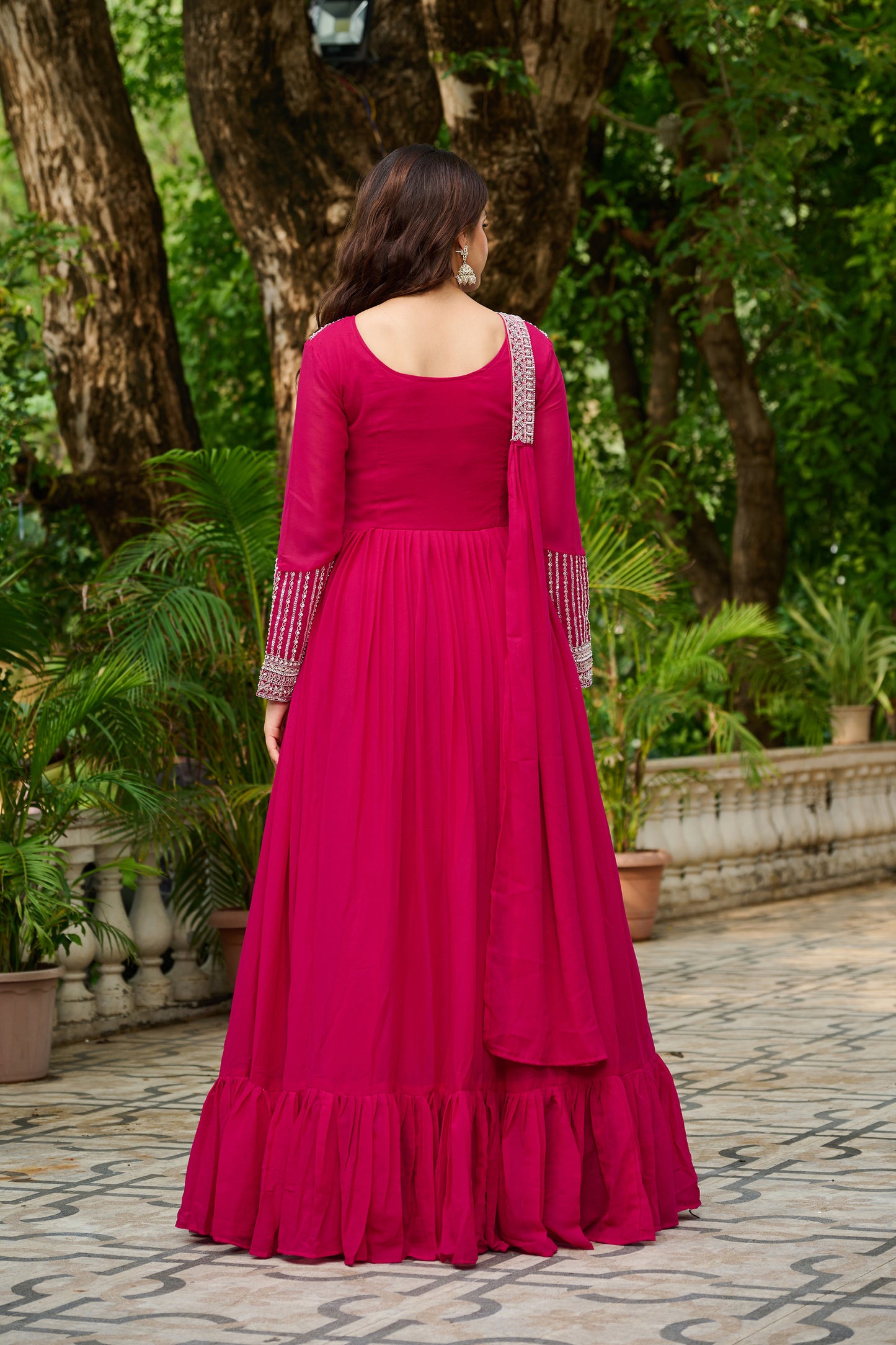 Woman in a pink traditional outfit standing outdoors with greenery in the background
