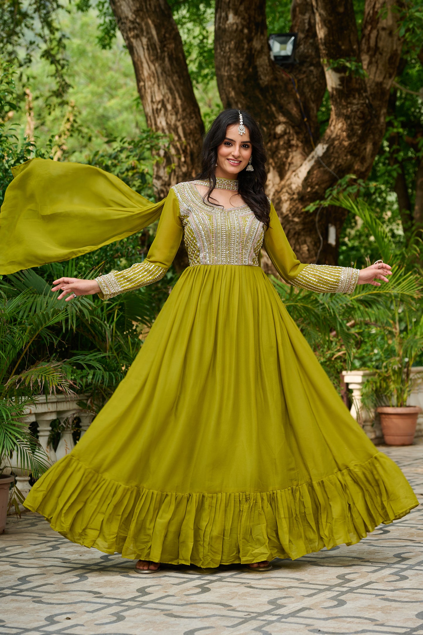 Woman in a green traditional outfit standing outdoors with trees in the background