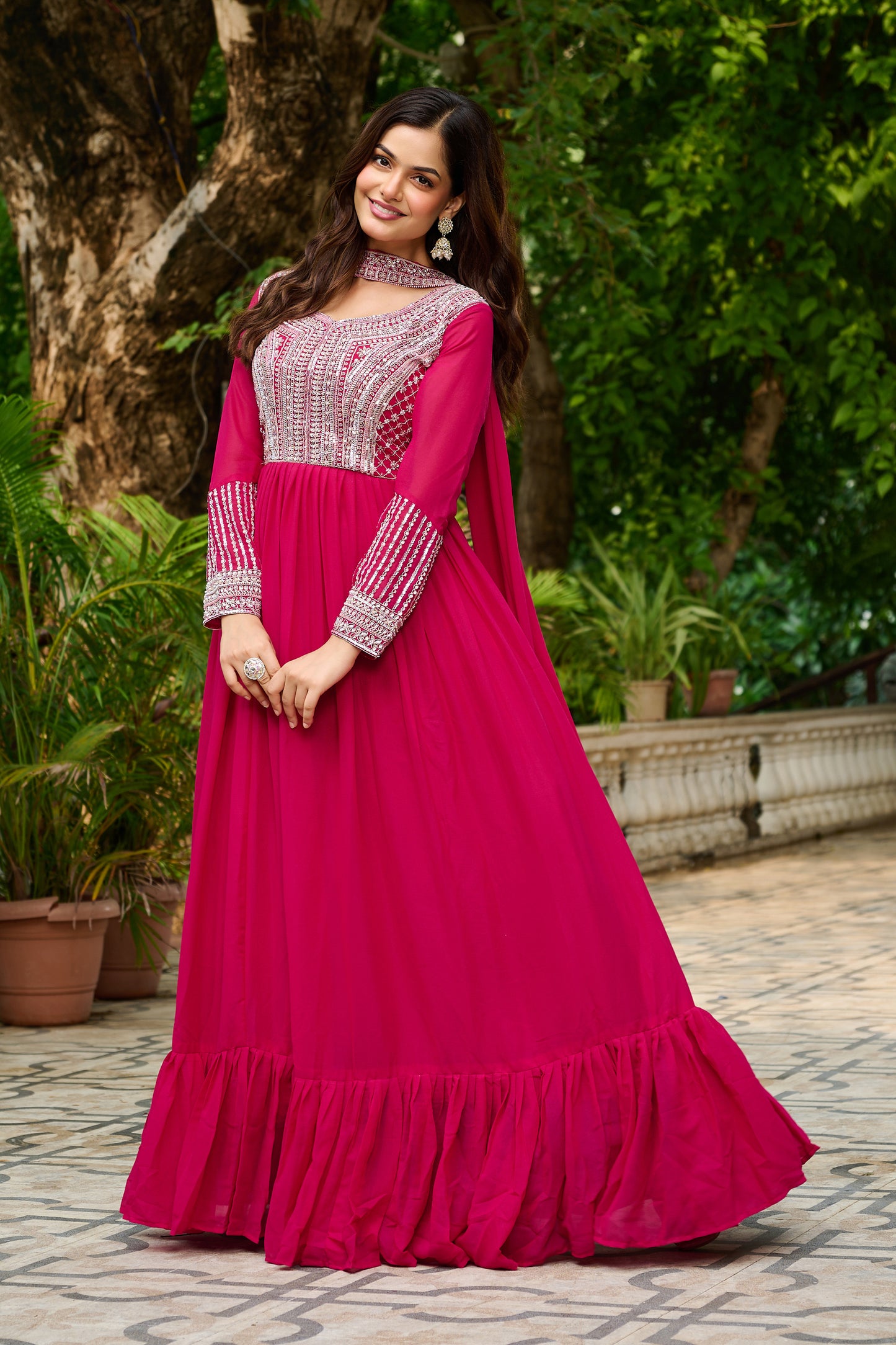Woman wearing a pink traditional outfit with a white embroidered top, standing outdoors.