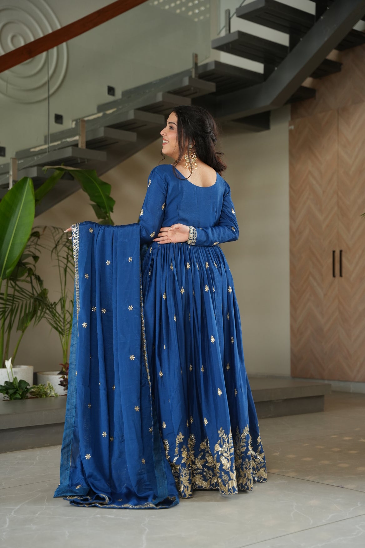 Woman wearing a blue traditional outfit with gold patterns indoors.