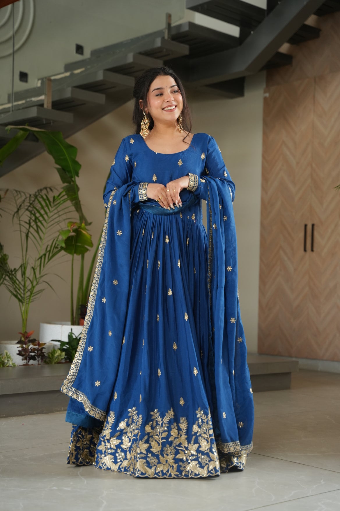 Woman wearing a blue traditional outfit with gold embroidery indoors.