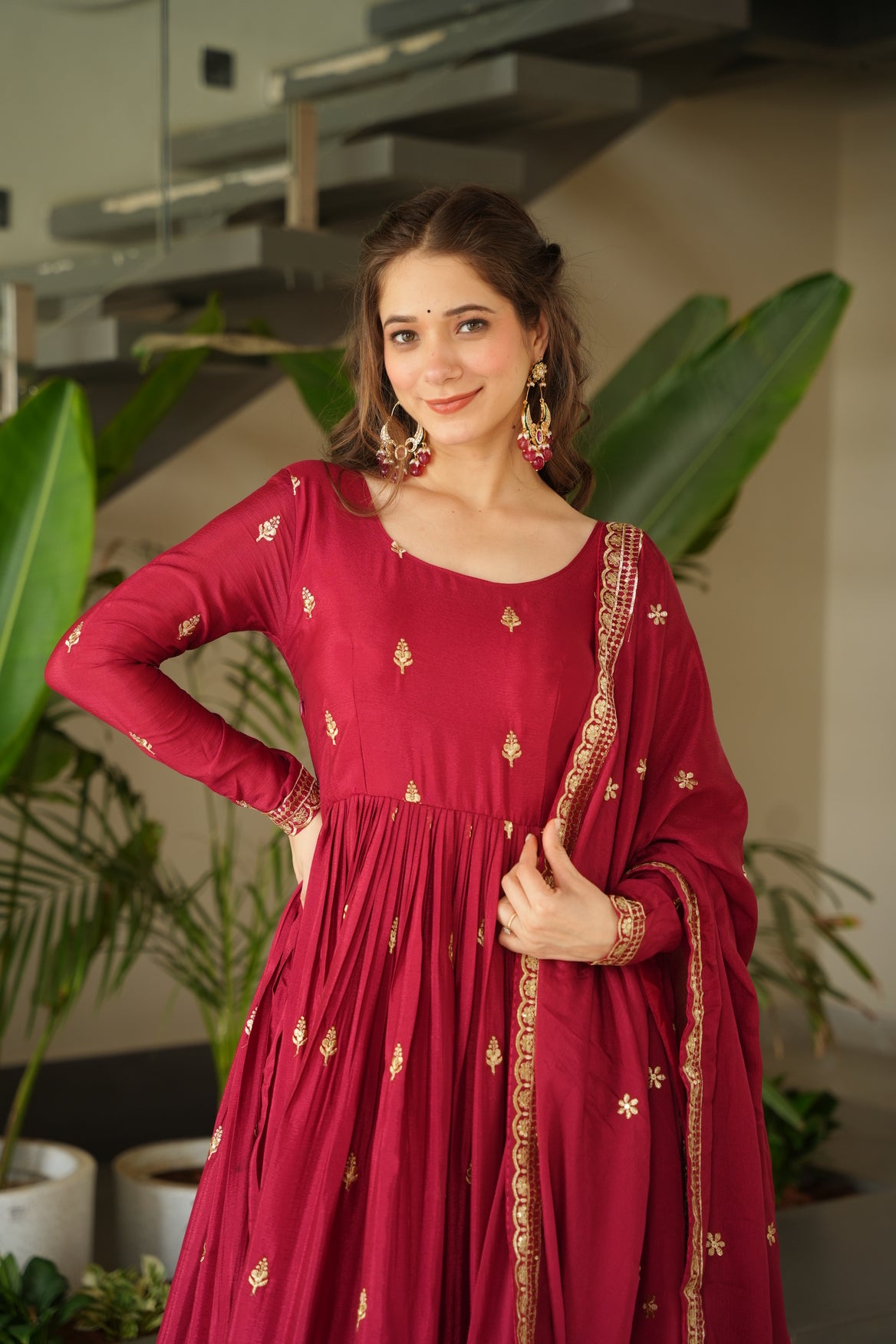 Woman wearing a red traditional outfit with gold embroidery indoors.