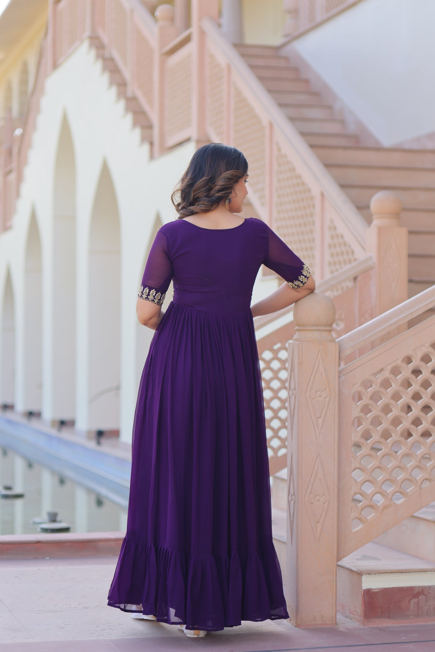 Woman in a purple dress standing on a staircase with a geometric wall design.