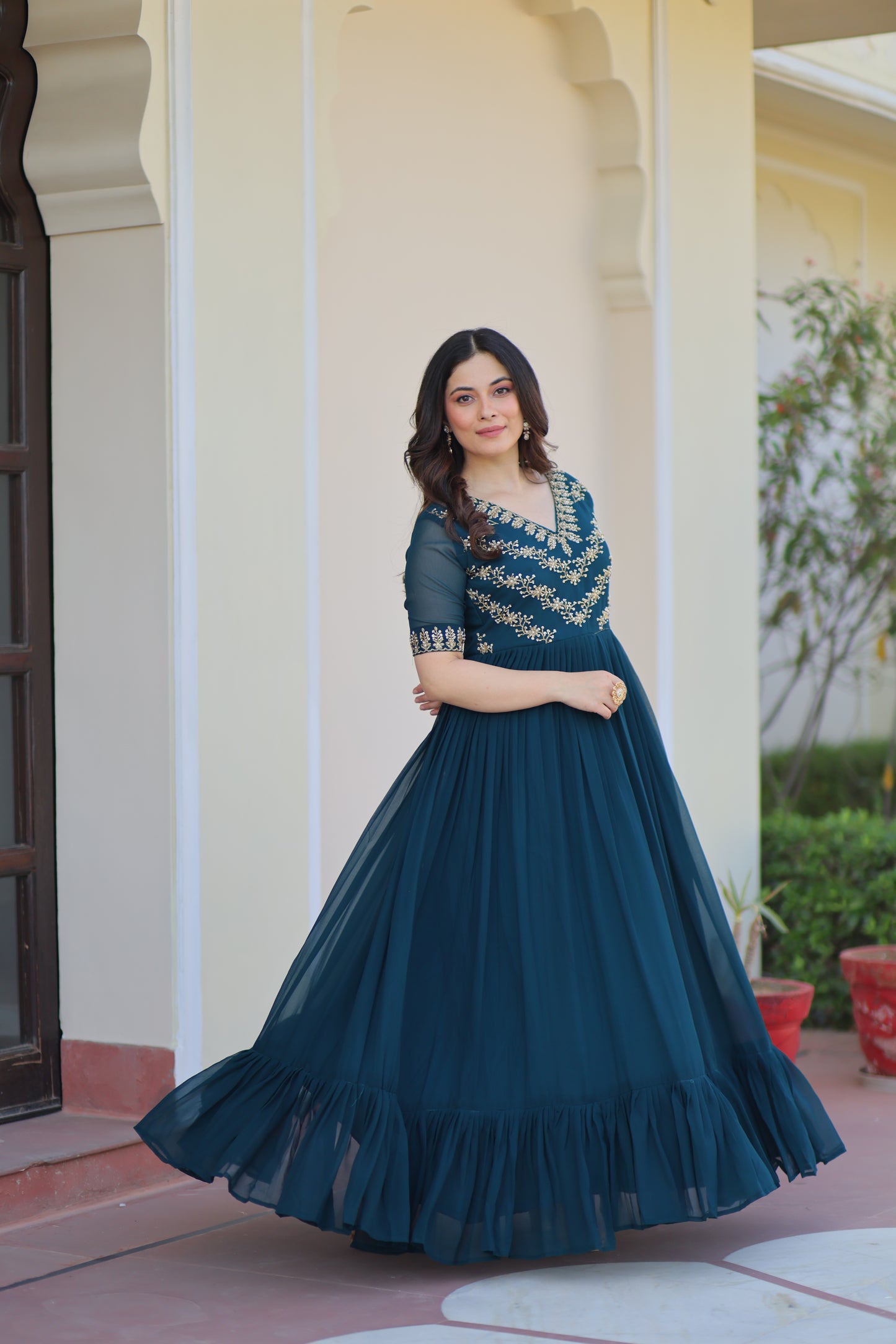 Woman in a blue dress standing against a white wall with a blurred background