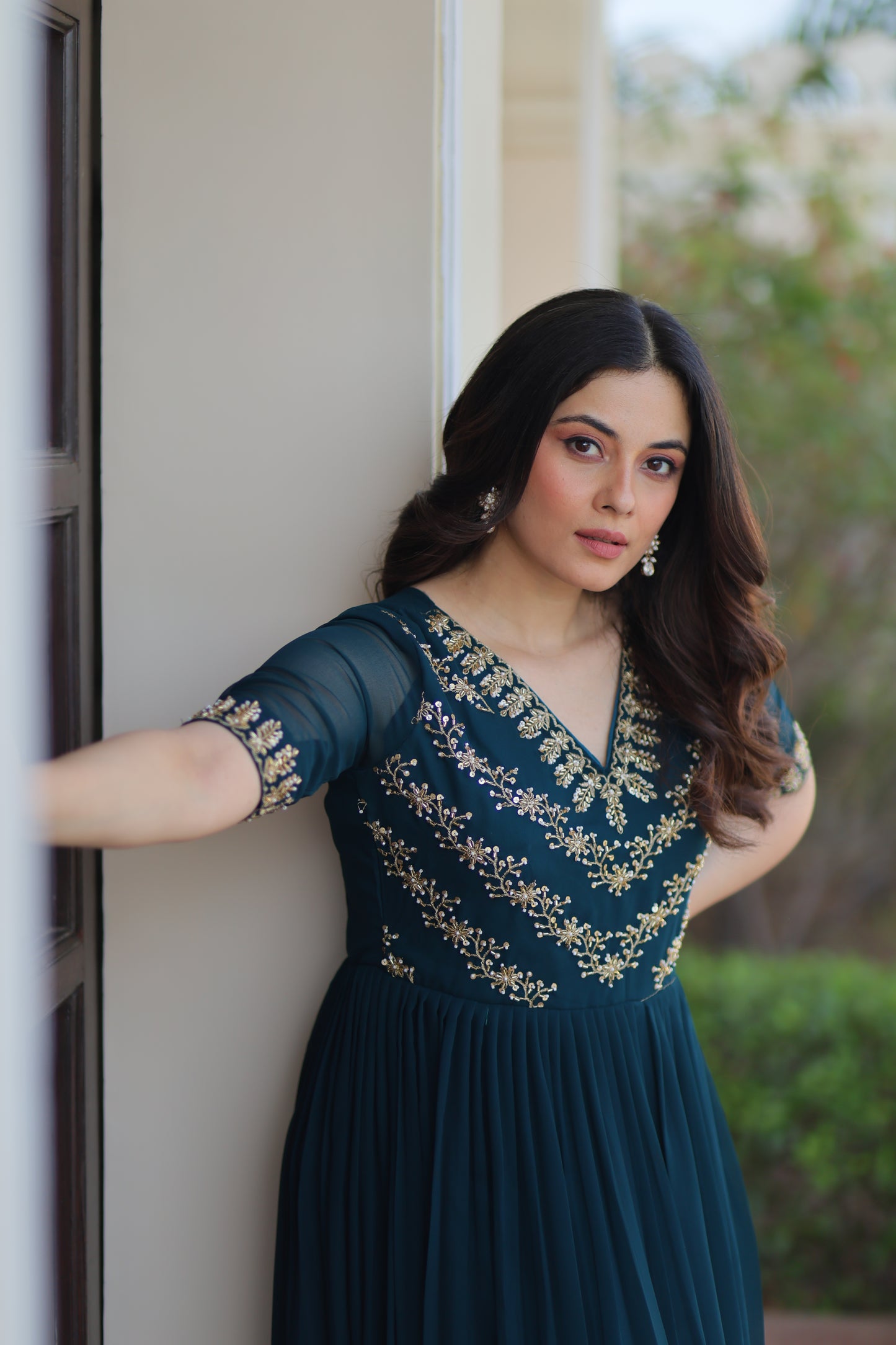 Woman in a blue dress with gold embroidery standing against a neutral background