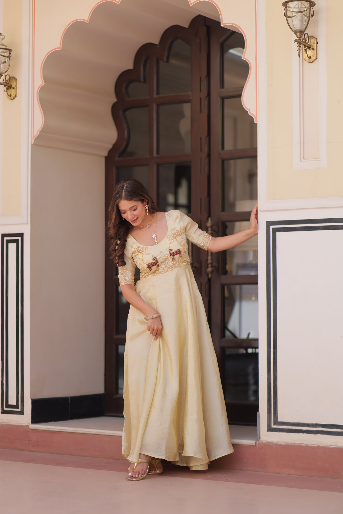 Woman in a long, light-colored dress standing on a balcony with decorative railings.