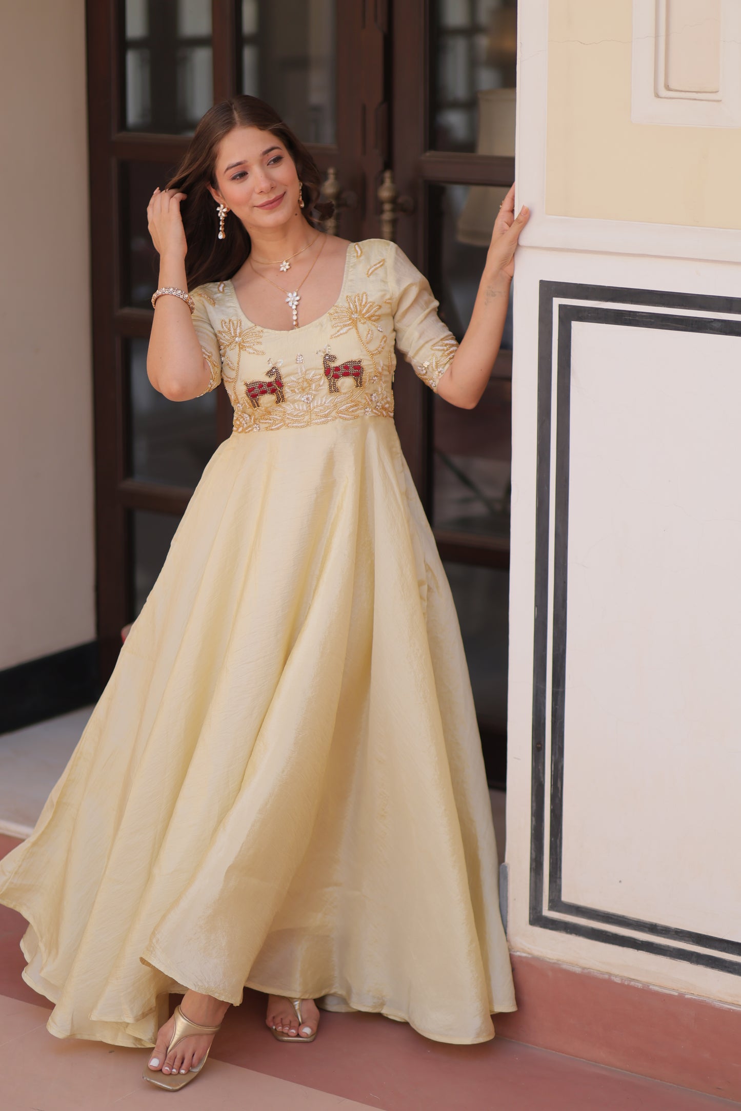 Woman in a beige evening gown standing next to a decorative wall.