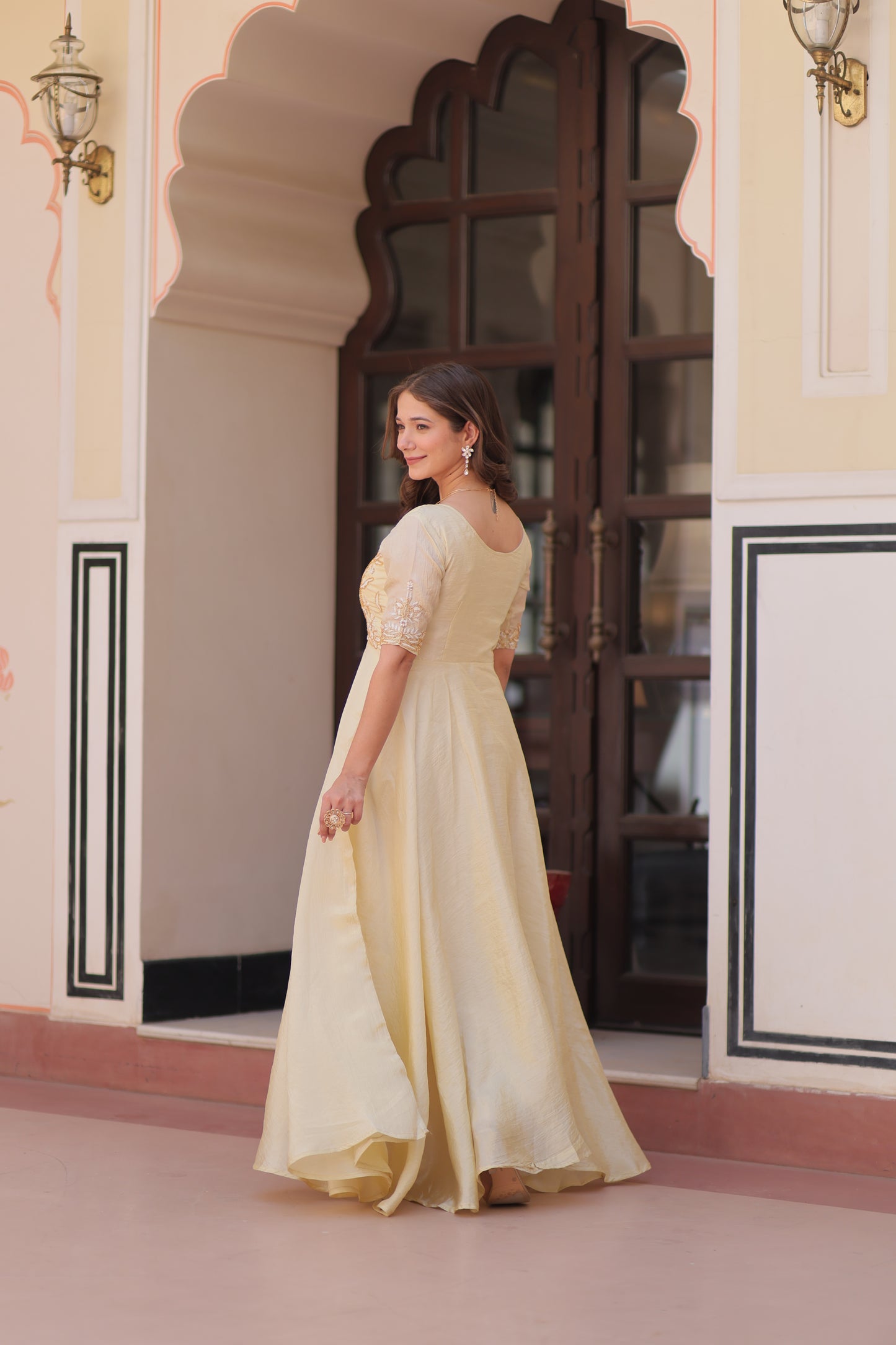 Woman in a light-colored dress standing in front of a mirror, adjusting her dress.