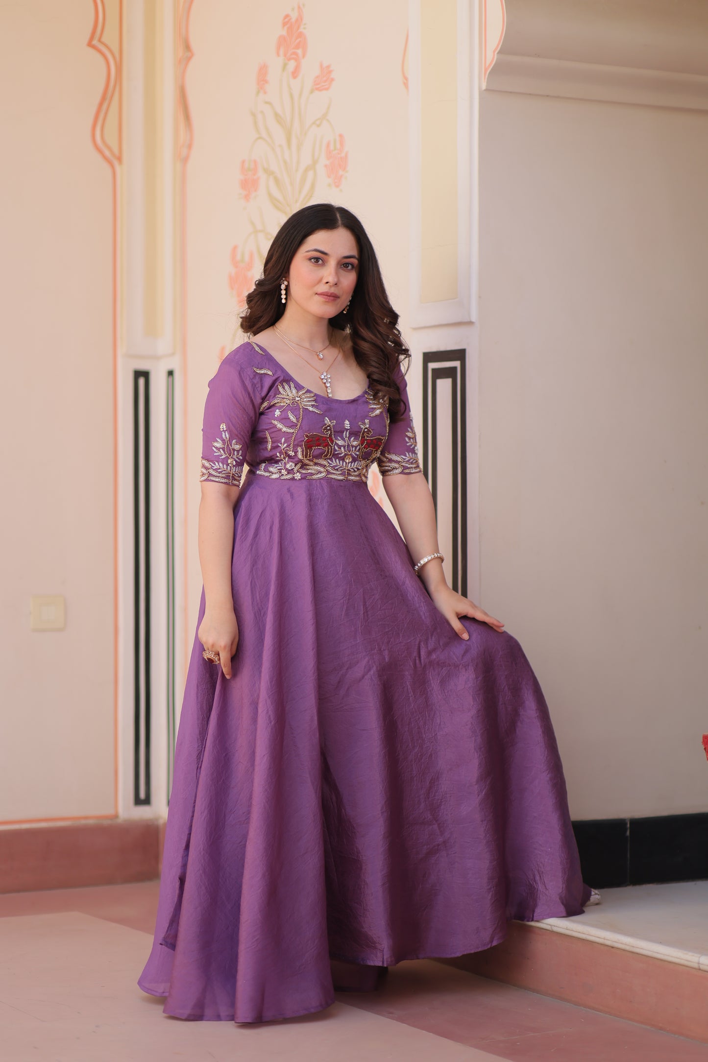 Woman wearing a purple dress with floral embroidery in a room.