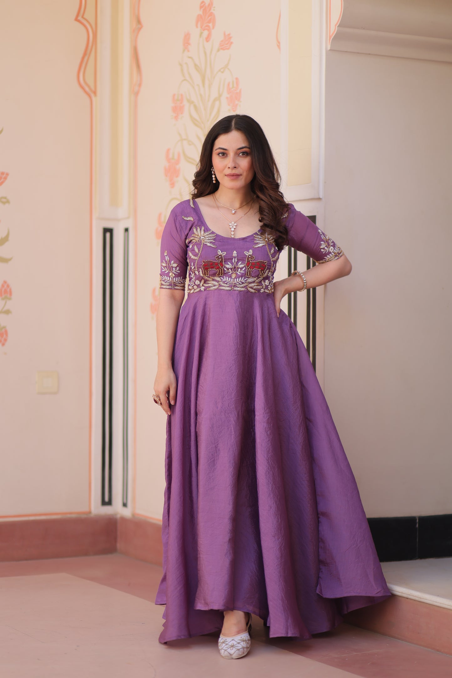 Woman in a purple dress with floral patterns standing indoors.