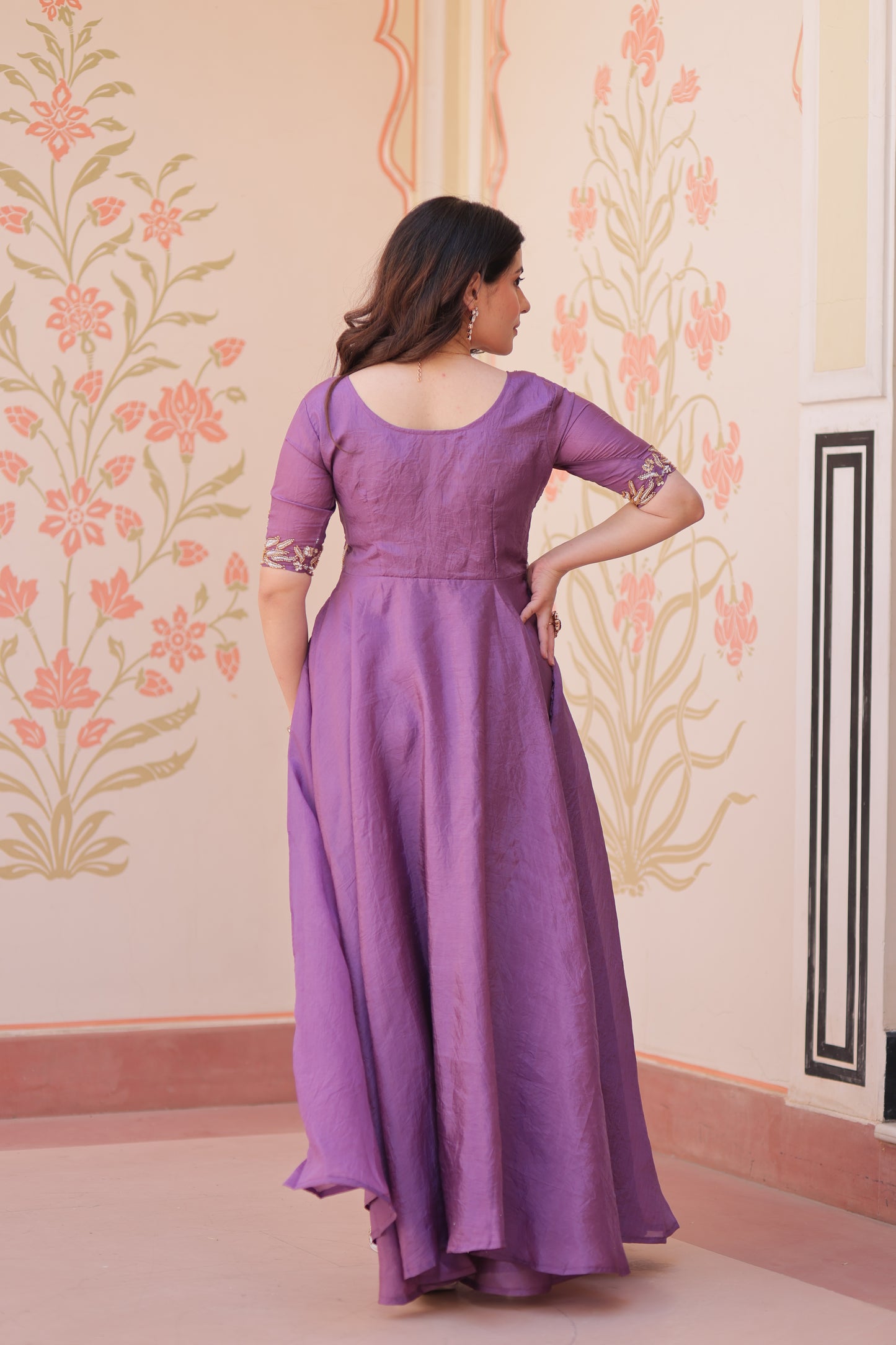 Woman in a purple dress standing against a floral decorated wall.