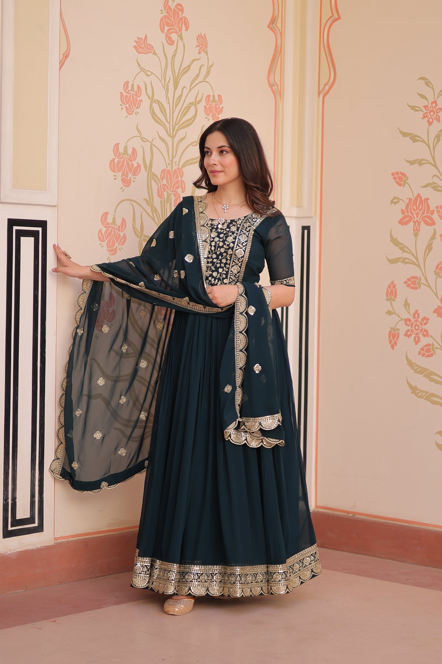 Woman wearing a dark blue traditional outfit with intricate patterns in a decorated room.