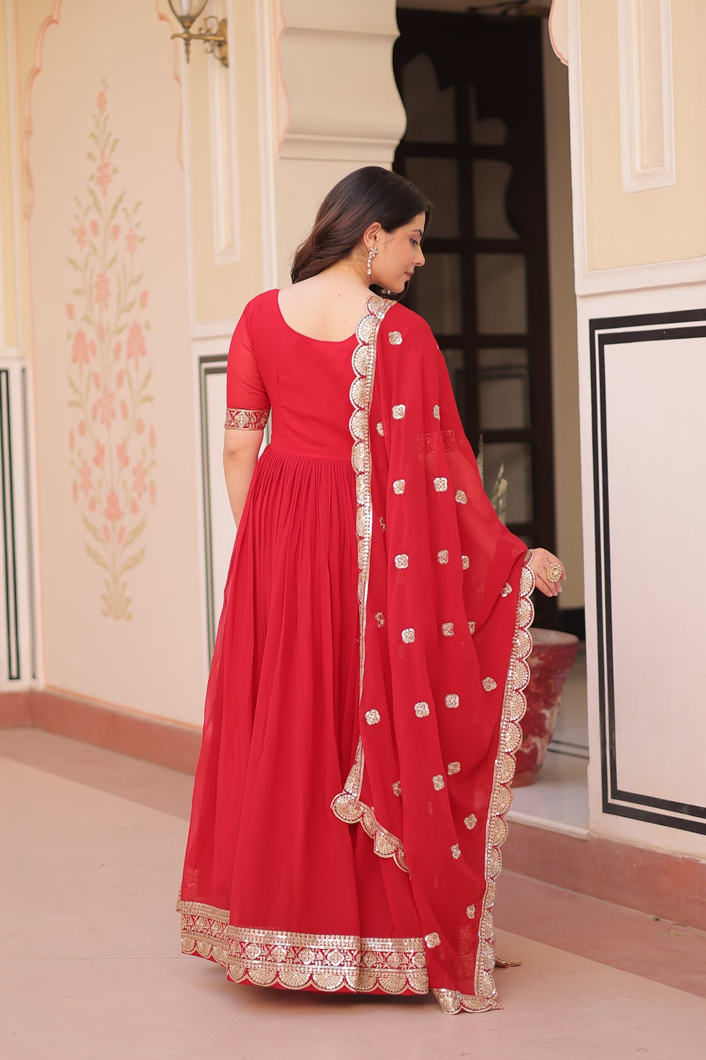 Woman wearing a red traditional outfit with white patterns indoors.