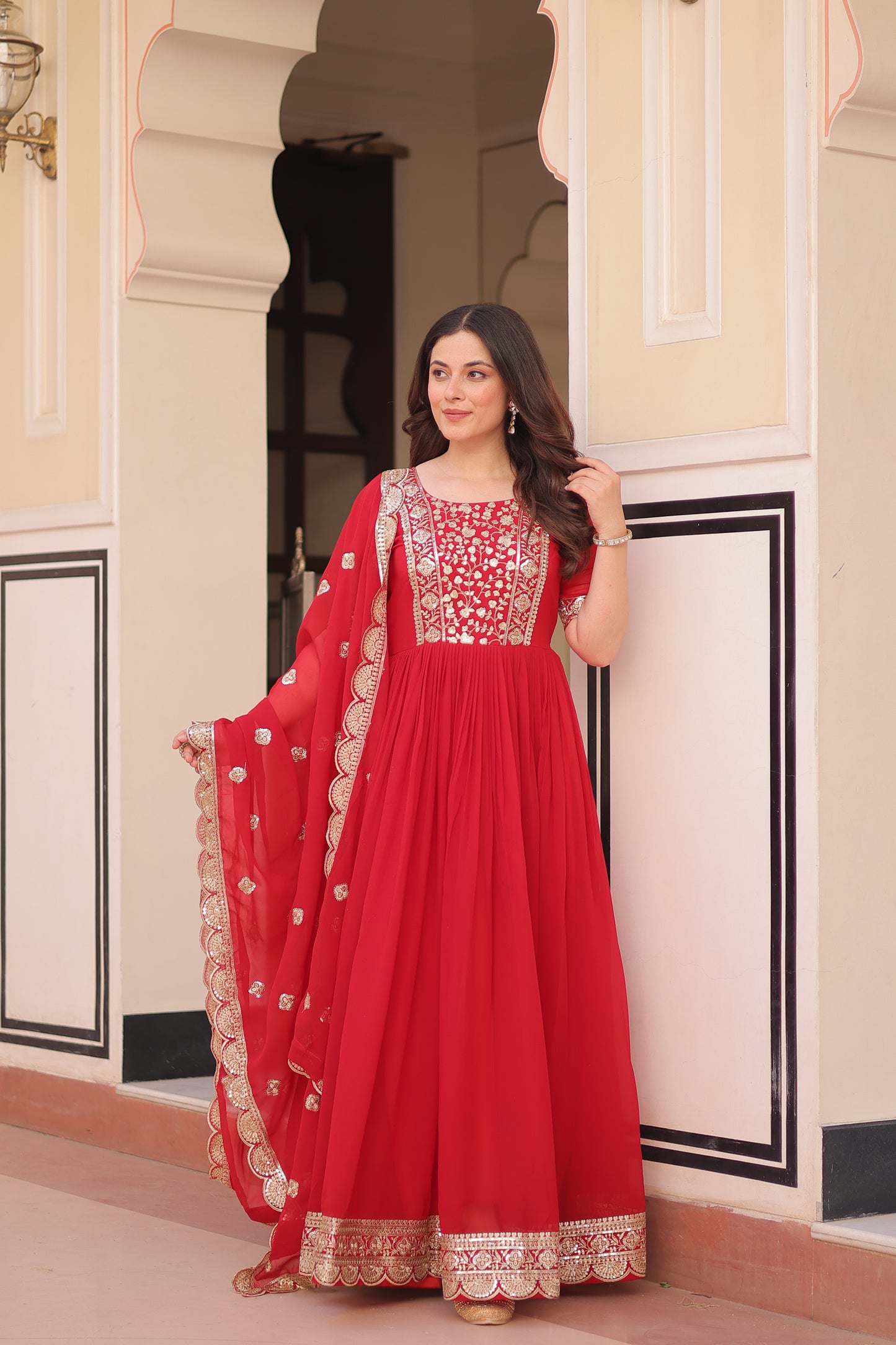 Woman wearing a red traditional outfit with gold embroidery in an indoor setting.
