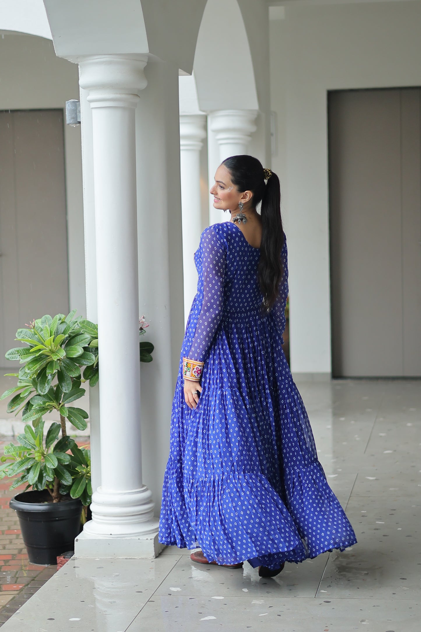 Woman in a blue dress standing in front of white columns with a plant in the background