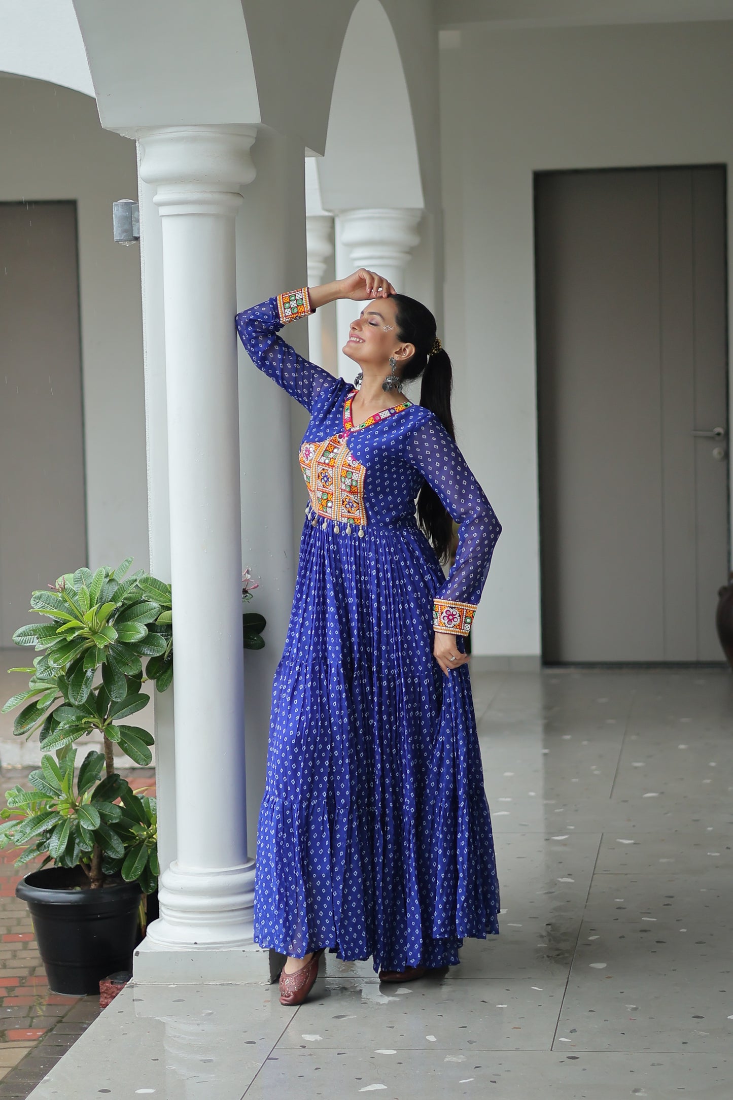 Woman in a blue dress with patterns standing in front of a white column.