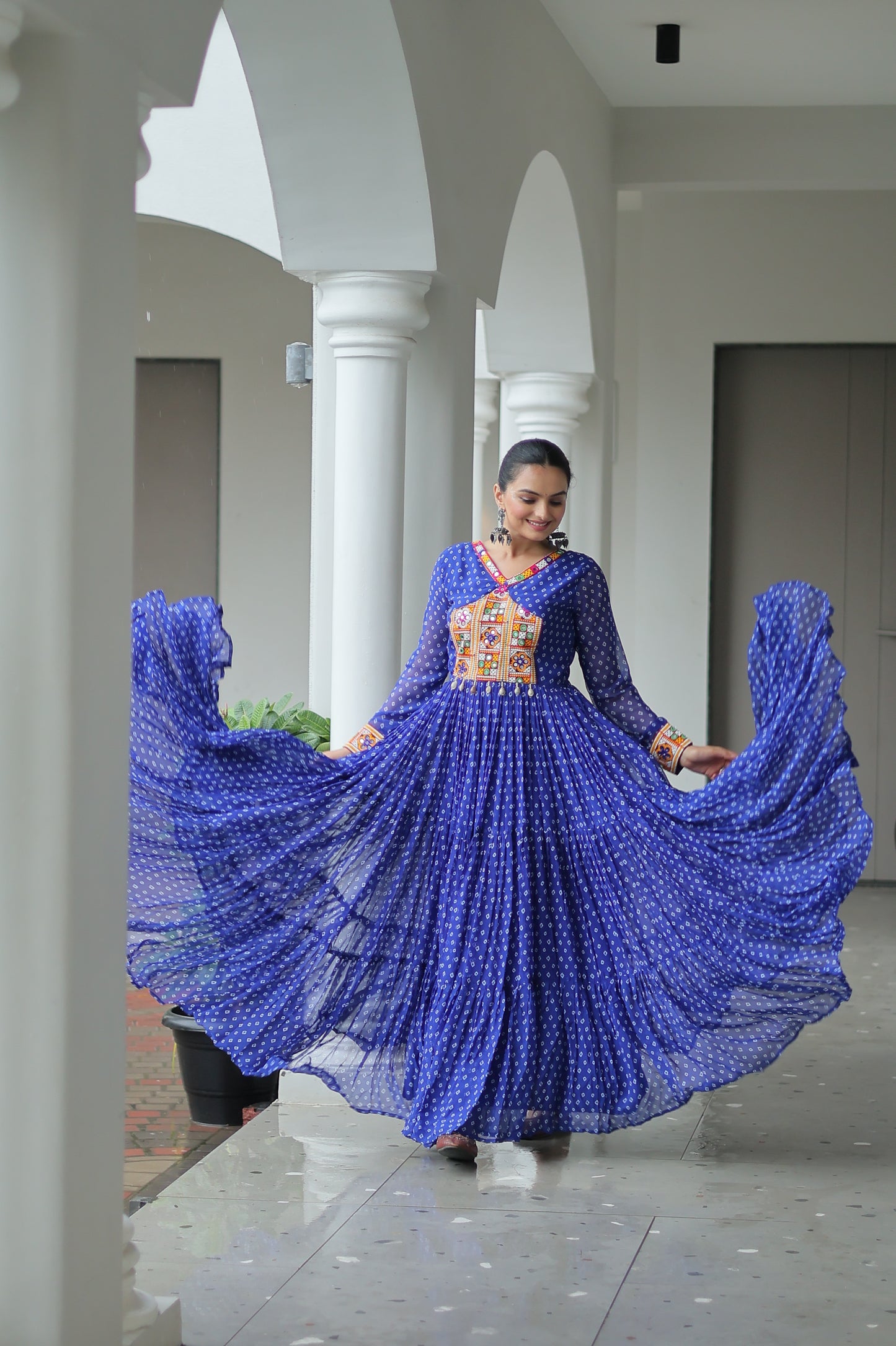 Woman in a blue dress with a patterned design standing in a modern indoor setting.