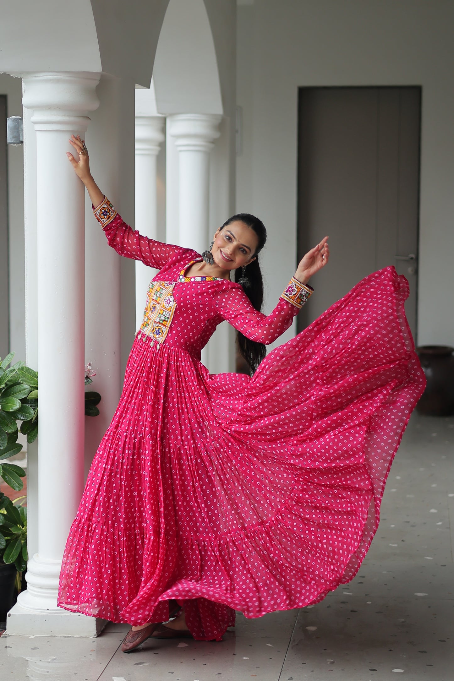 Woman in a bright pink traditional outfit with a long skirt, standing indoors.