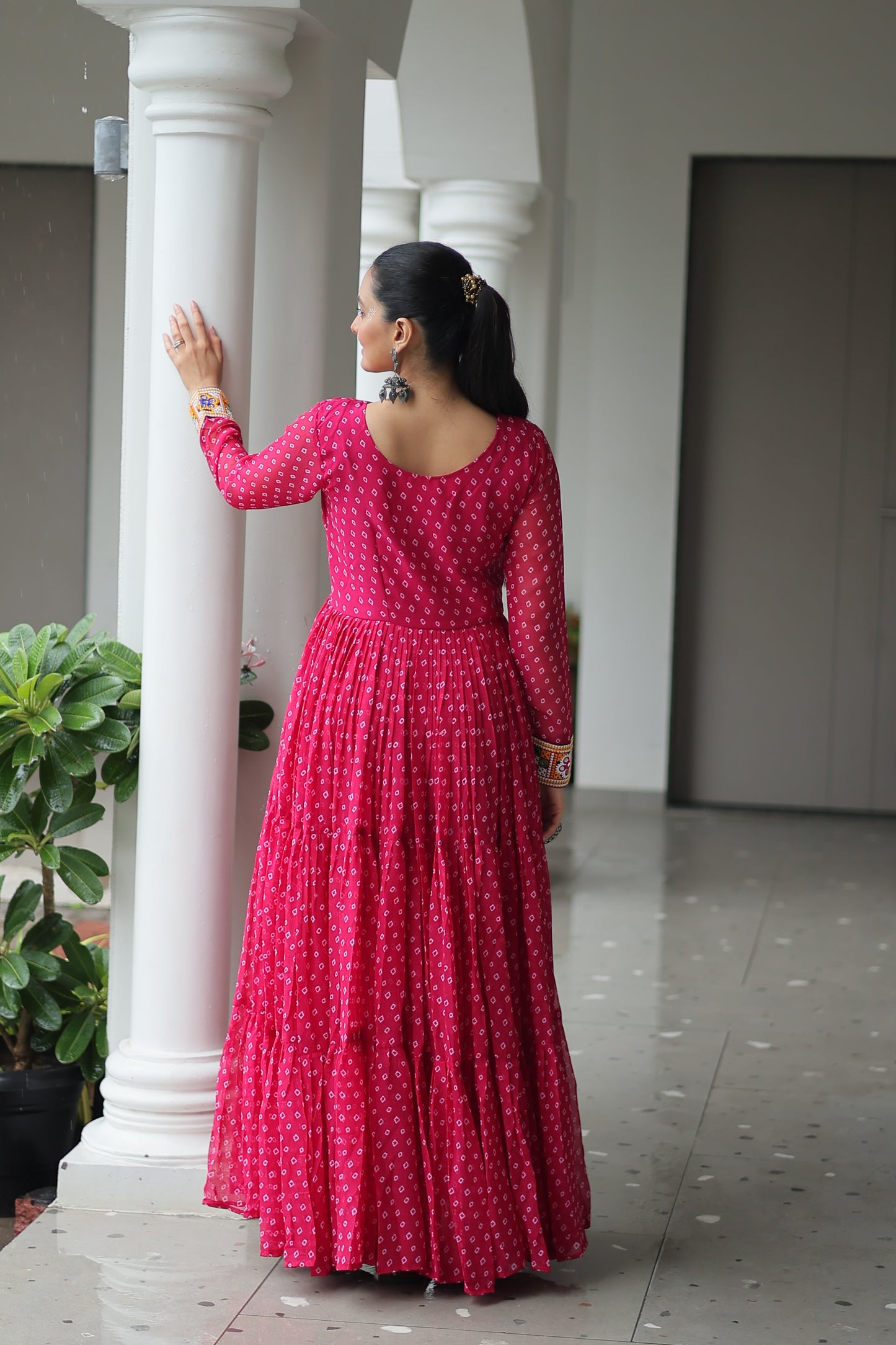 Woman in a pink polka dot dress standing against a white column.