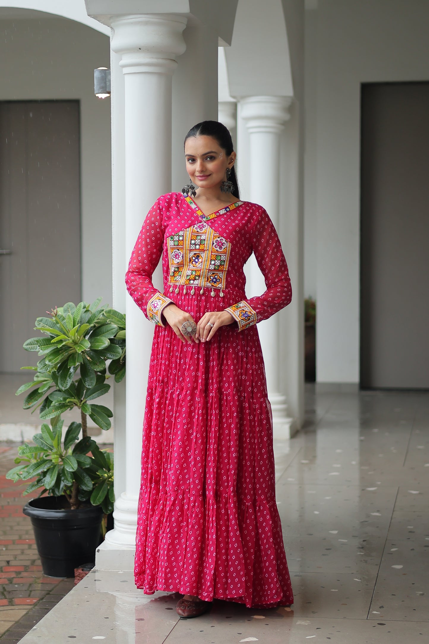 Woman wearing a pink traditional outfit with intricate patterns in an indoor setting.