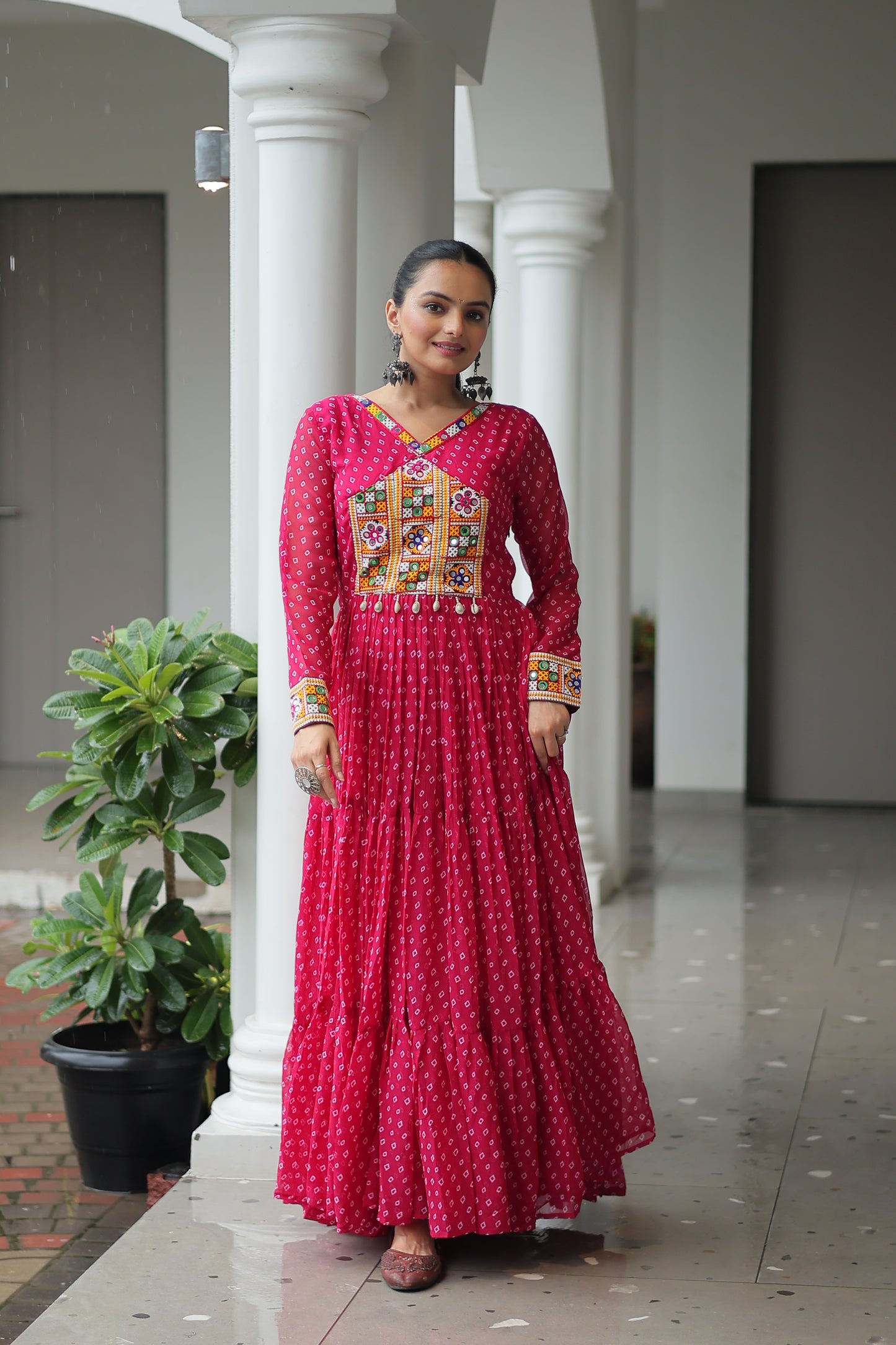 Woman in a red traditional outfit standing on a staircase with plants in the background