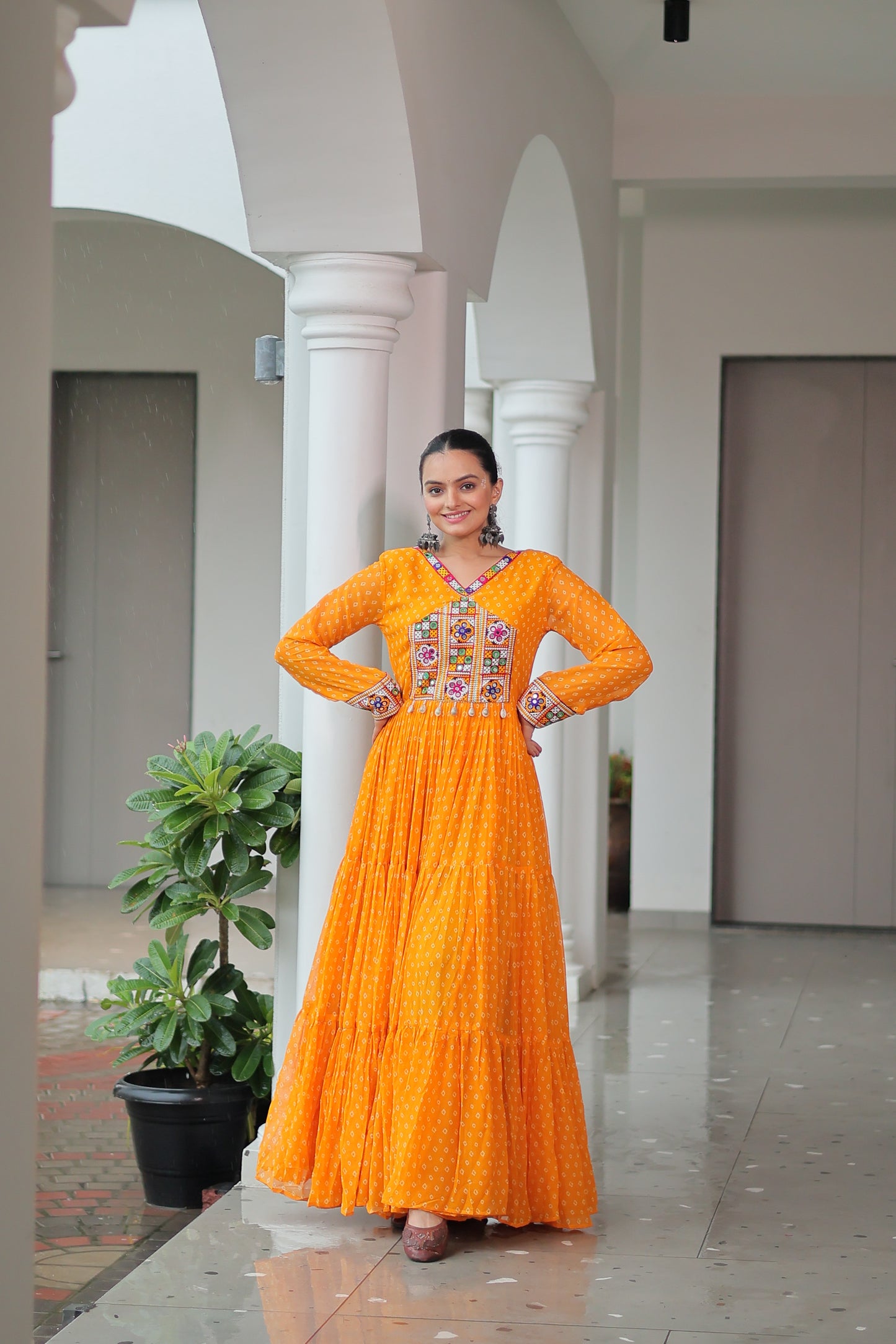 Woman in an orange dress with floral patterns standing indoors.